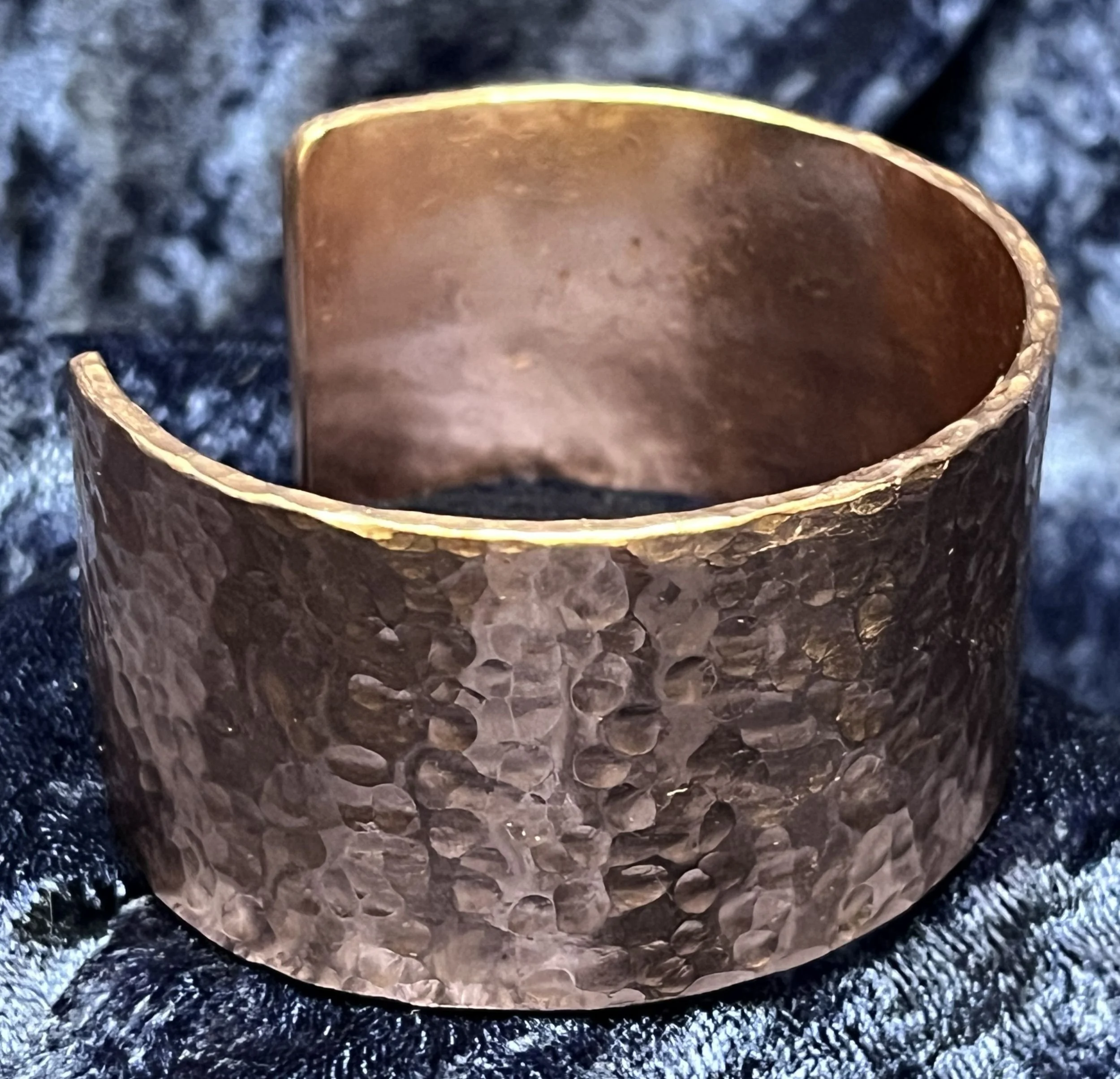 Hammered Copper bracelet laying on a blue background.