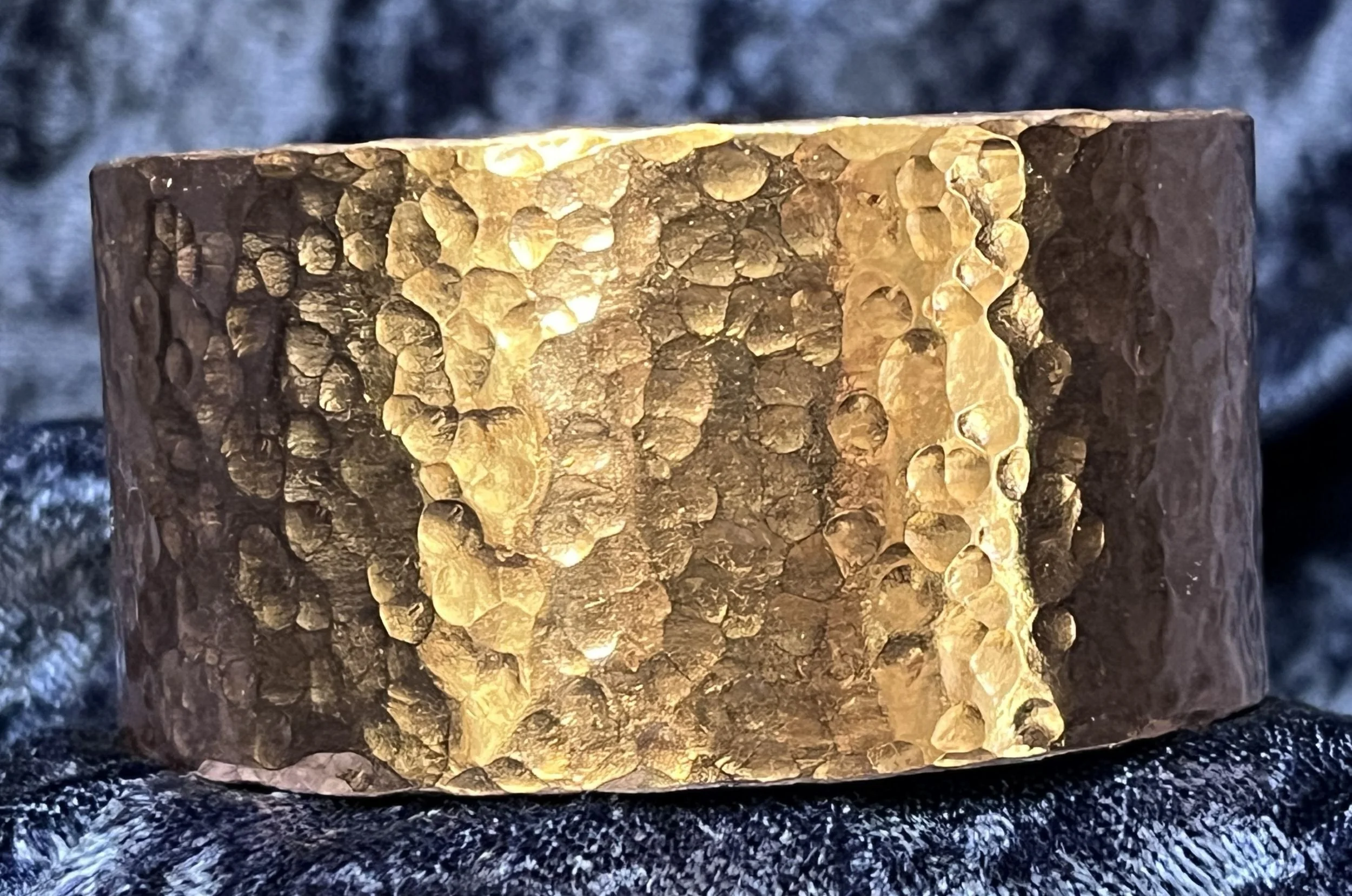 Hammered Copper bracelet laying on a blue background.