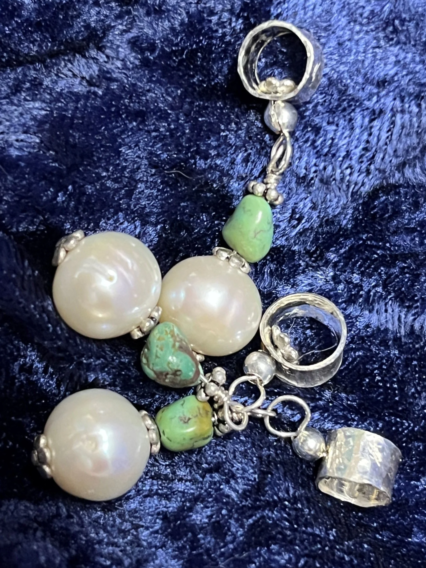 Pile of pearl and turquoise charms laying on blue background.