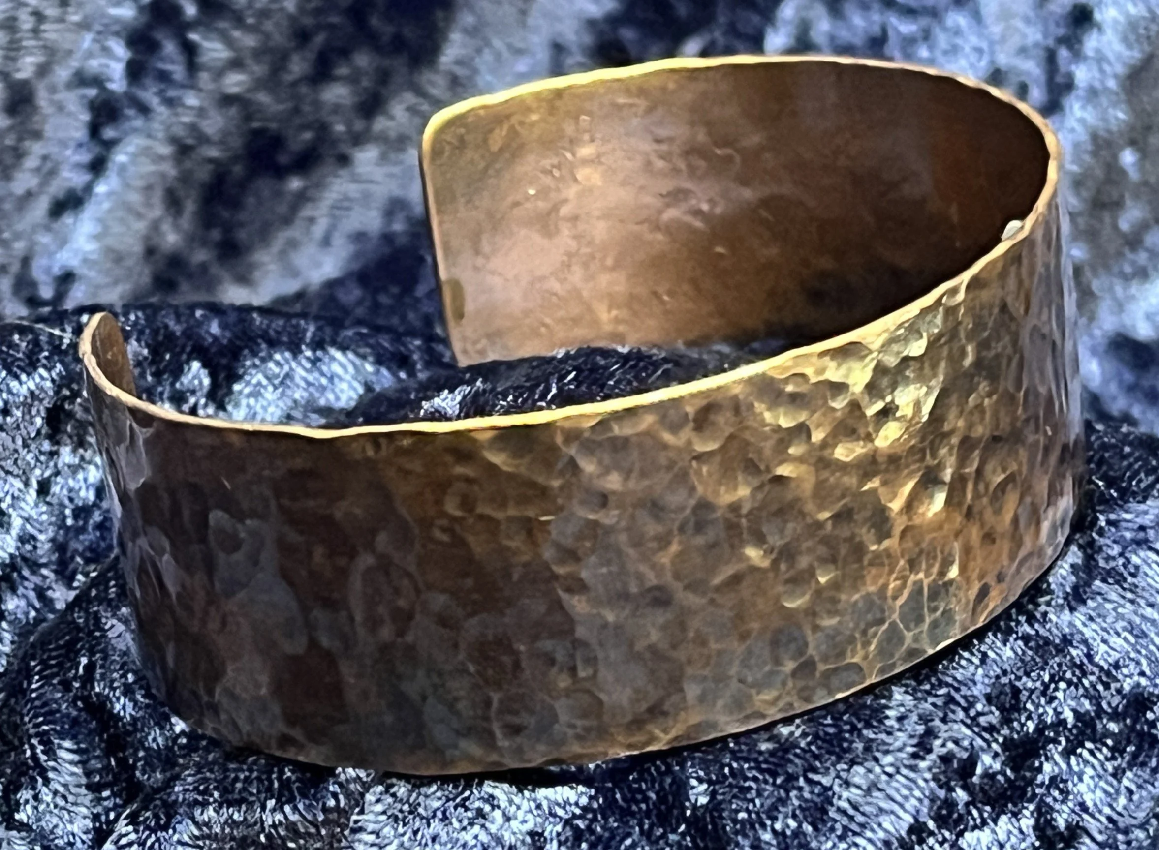 Hammered Copper bracelet laying on a blue background.