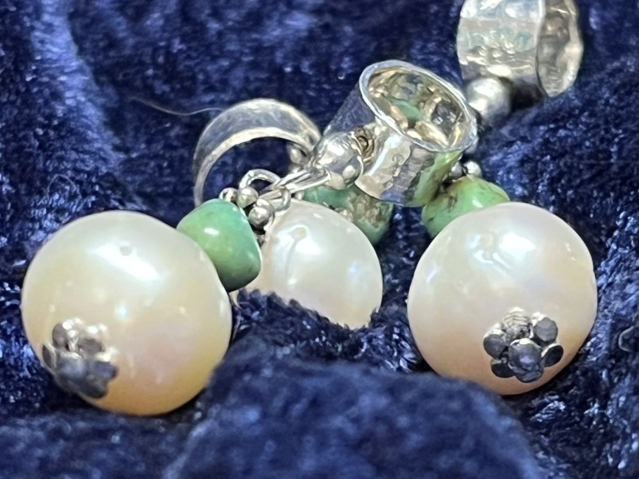 Pile of pearl and turquoise charms laying on blue background.