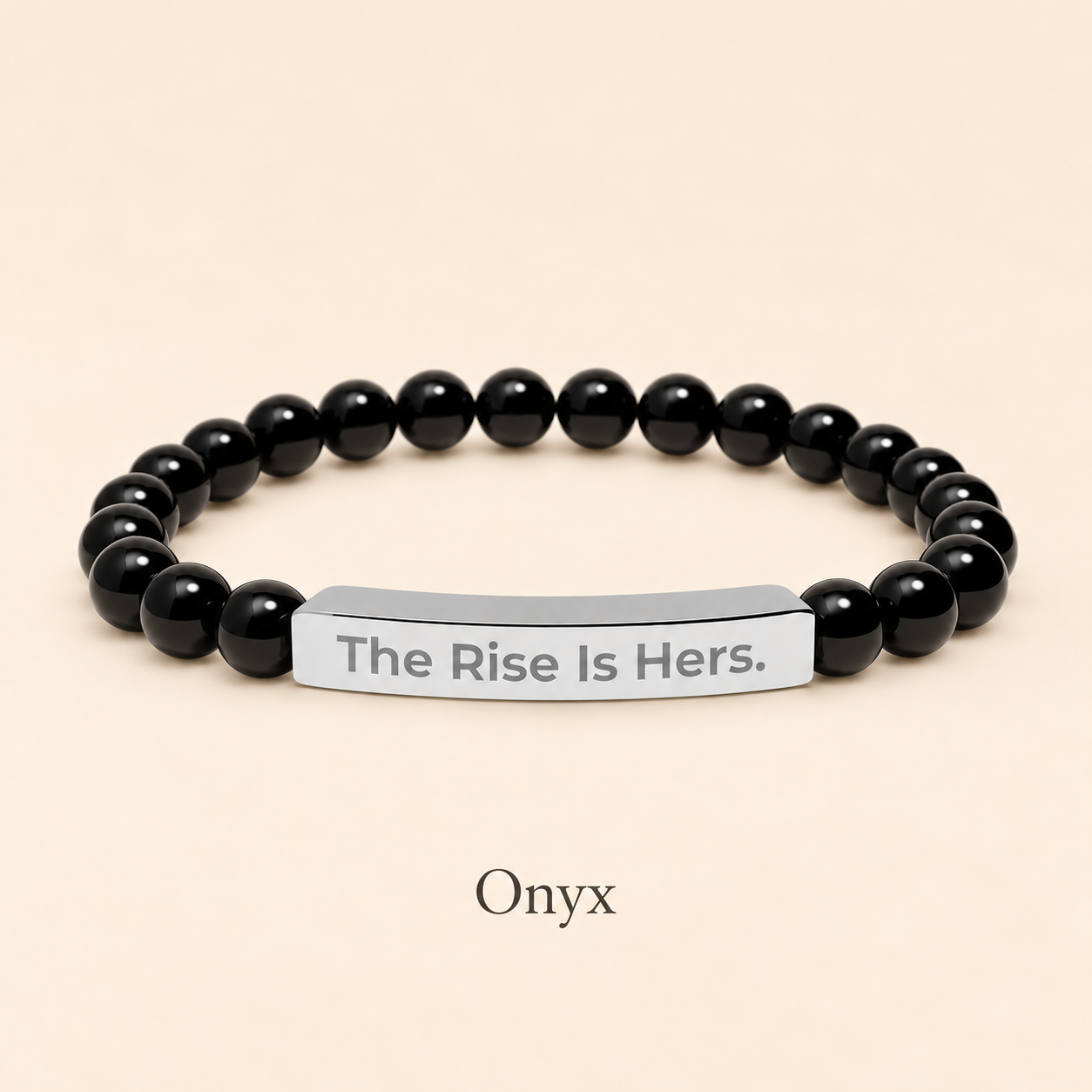 Onyx beaded stretch bracelet with a silver-tone bar engraved with The Rise Is Hers, displayed on an ivory background.