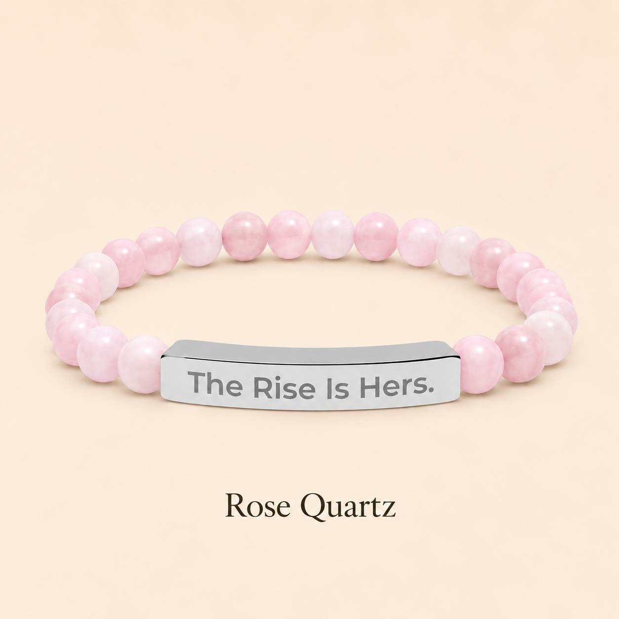 Rose Quartz beaded stretch bracelet with a silver-tone bar engraved with The Rise Is Hers, displayed on an ivory background.