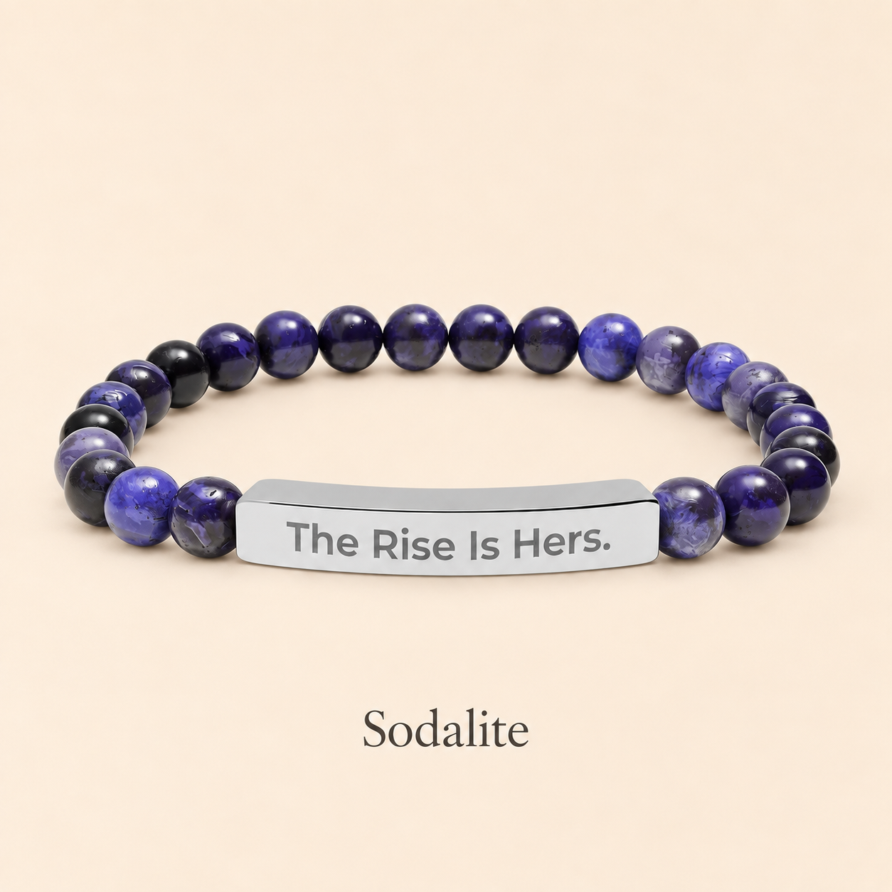 Sodalite beaded stretch bracelet with a silver-tone bar engraved with The Rise Is Hers, displayed on an ivory background.