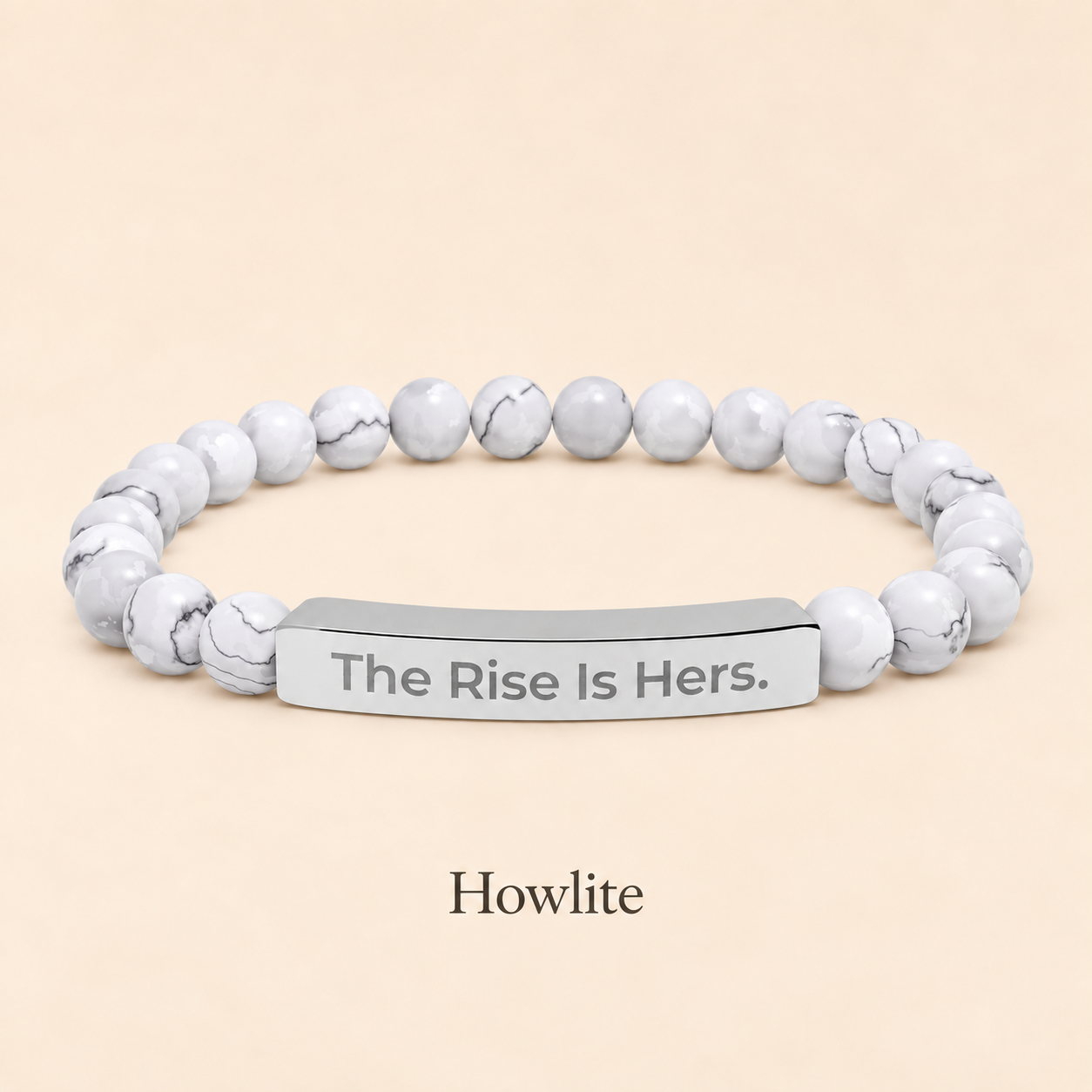 Howlite beaded stretch bracelet with a silver-tone bar engraved with The Rise Is Hers, displayed on an ivory background.
