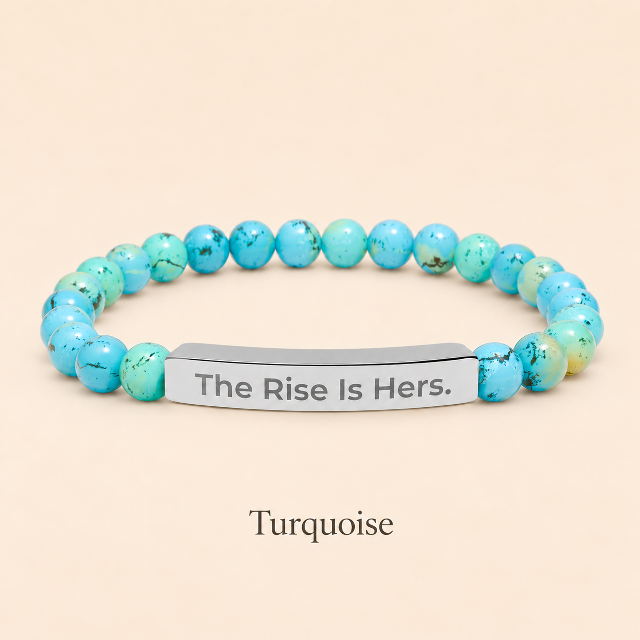 Turquoise beaded stretch bracelet with a silver-tone bar engraved with The Rise Is Hers, displayed on an ivory background.