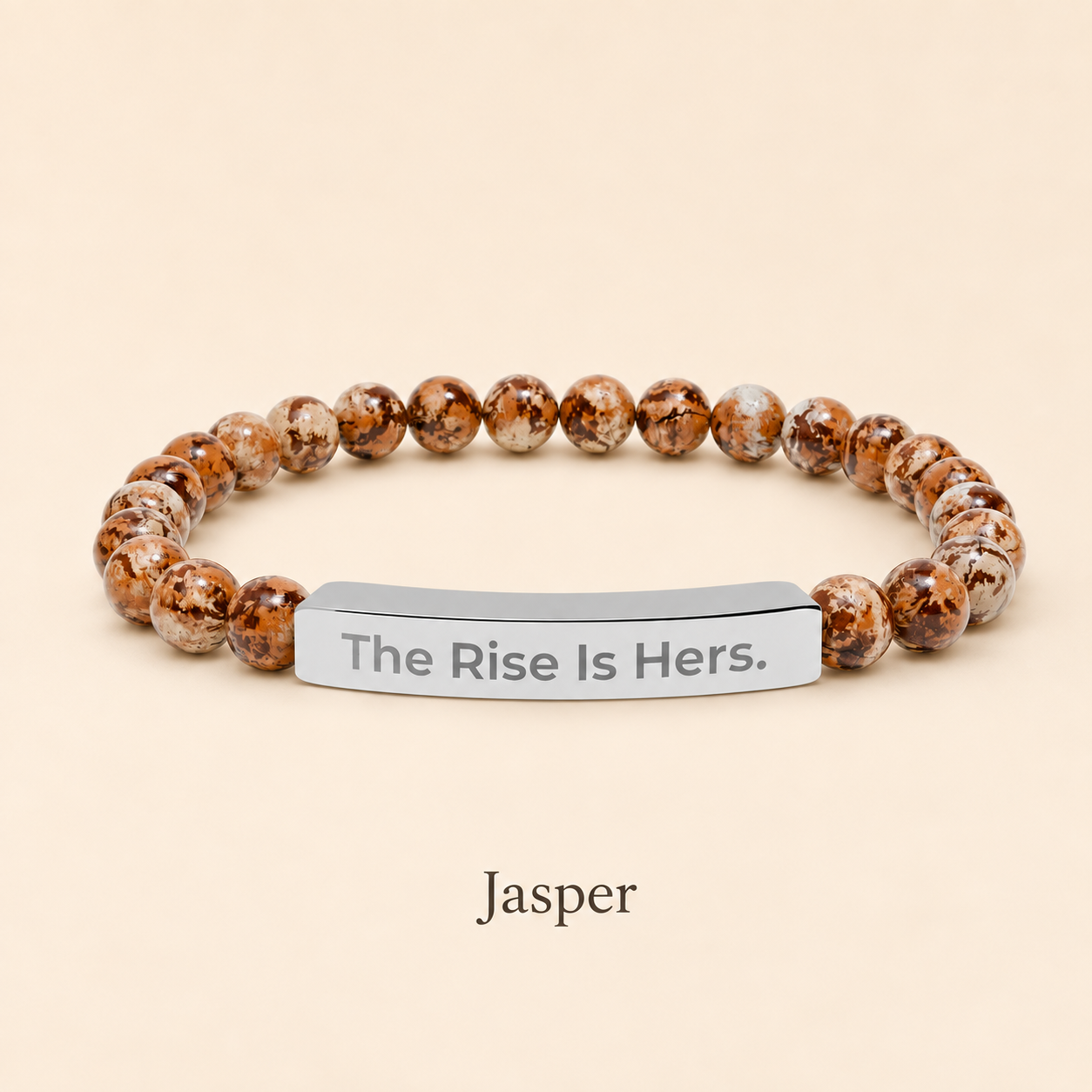 Jasper beaded stretch bracelet with a silver-tone bar engraved with The Rise Is Hers, displayed on an ivory background.