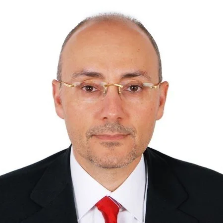 Professional portrait of a middle-aged man with glasses, wearing a suit and red tie against a white background.