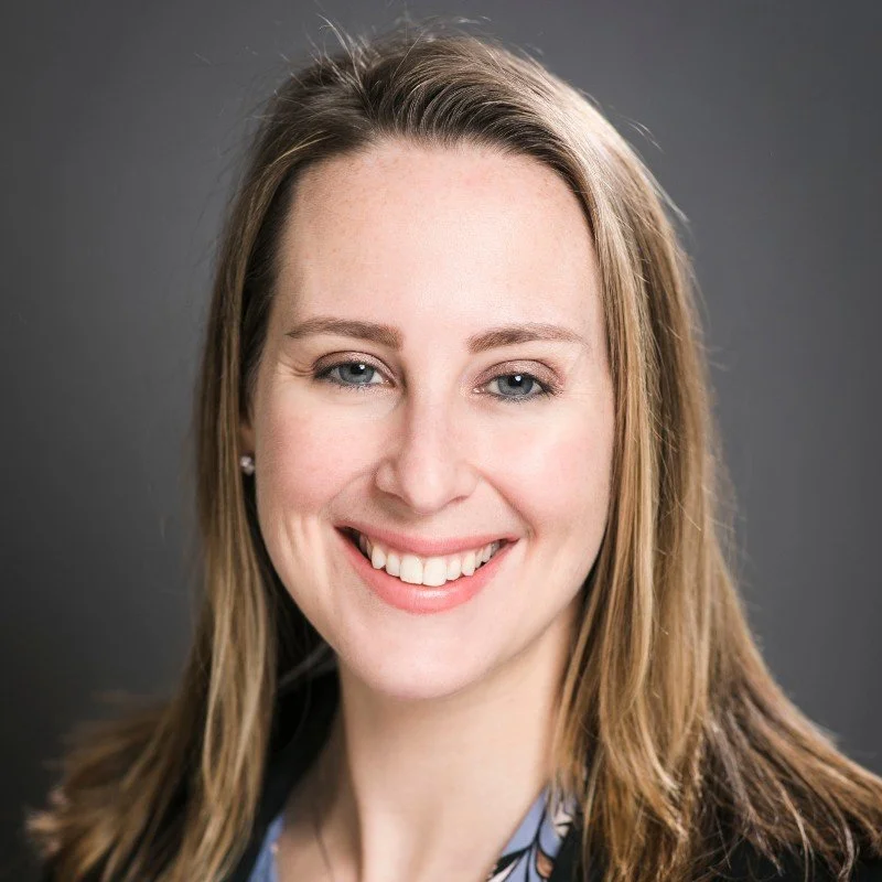 Close-up of smiling woman with long light brown hair and blue eyes against a dark background