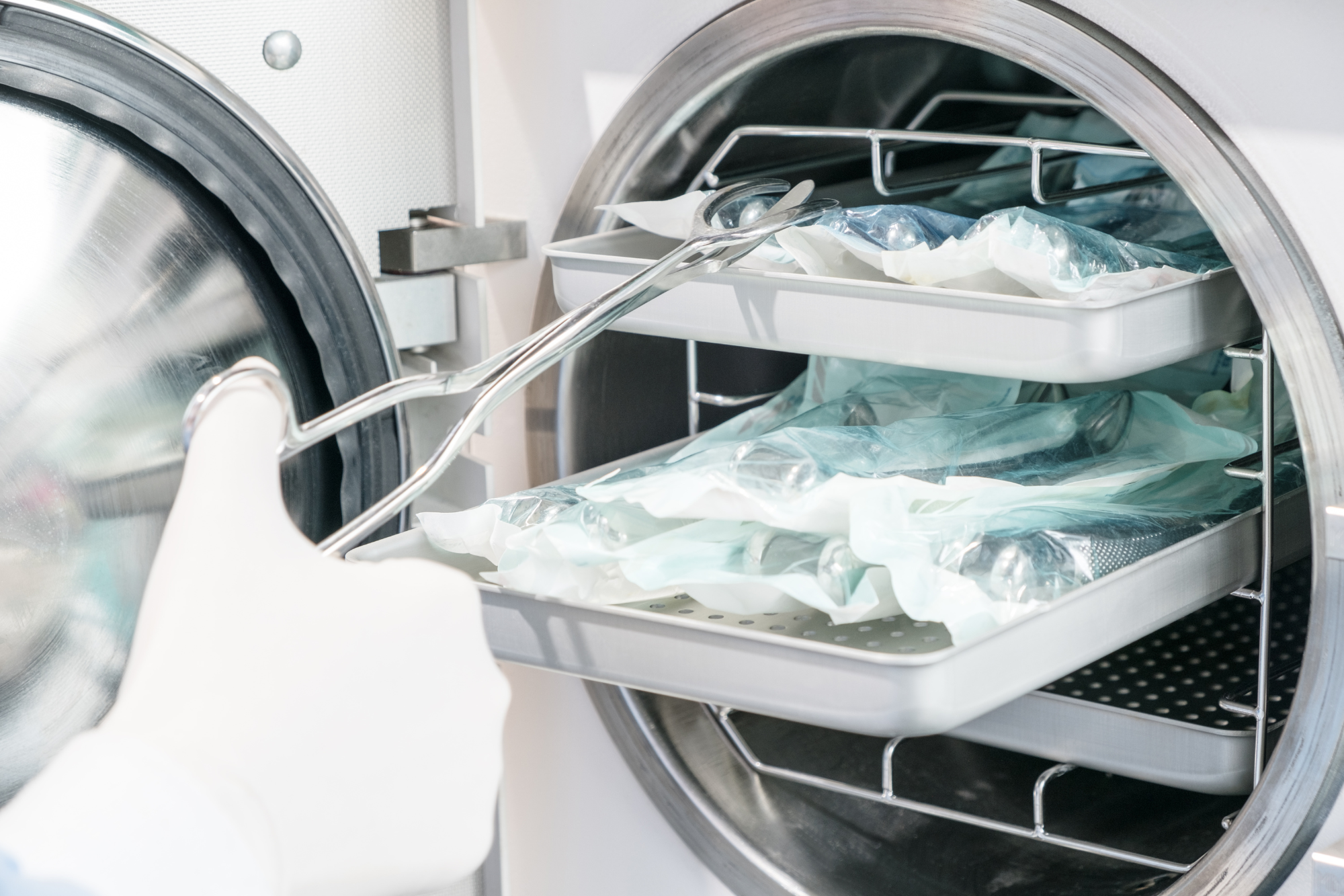 Inside a medical sterilization machine with open door, containing medical equipment and tools