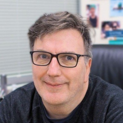 A man with glasses and gray hair smiling in an office setting.