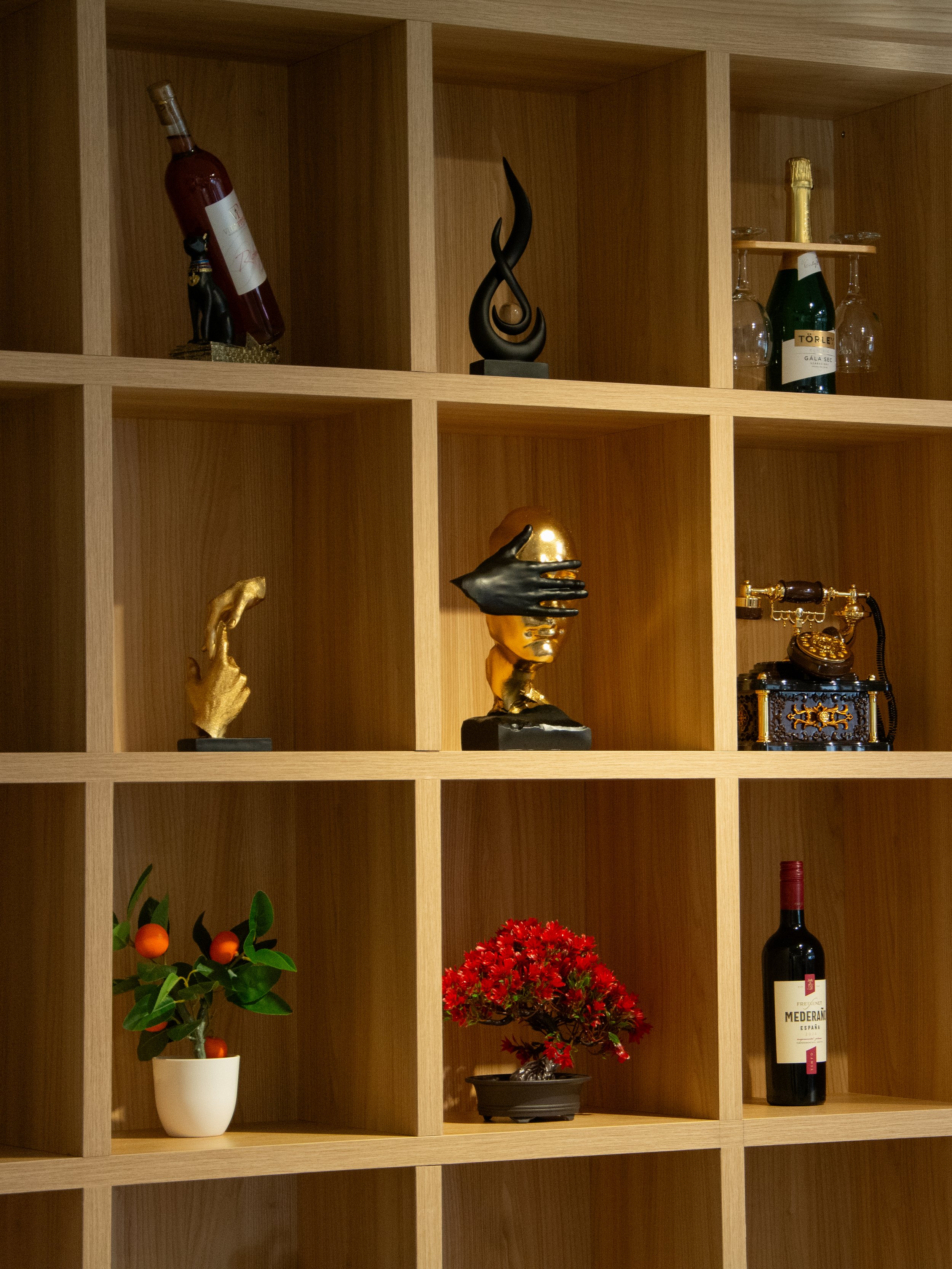 Wooden cubby shelf with various decorative items including a black sculpture, a wine bottle, a plant, and a red flowering plant.