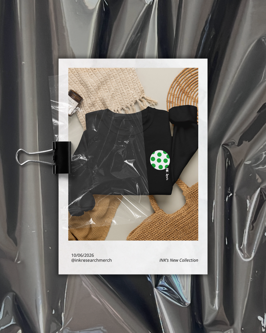 A polaroid-style photo of black clothing, a beige knit cloth, a small plant, and a woven bag, all displayed on a white surface, with a background of crinkled metallic material.