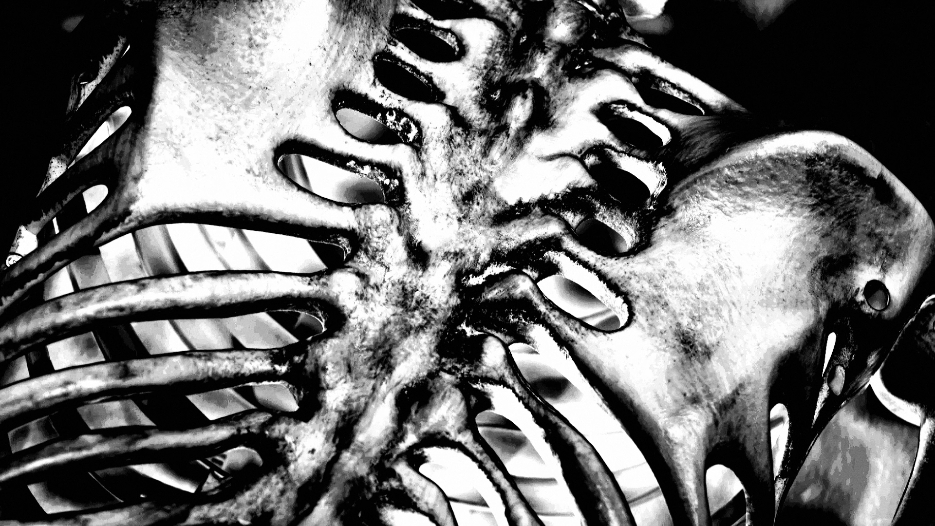Black and white close-up of a metal sculpture with multiple face-like openings and intricate, textured details.