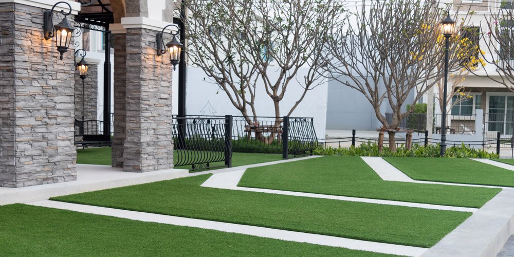 Empty outdoor patio with grass patterns, stone pillars, black lamp posts, and leafless trees.