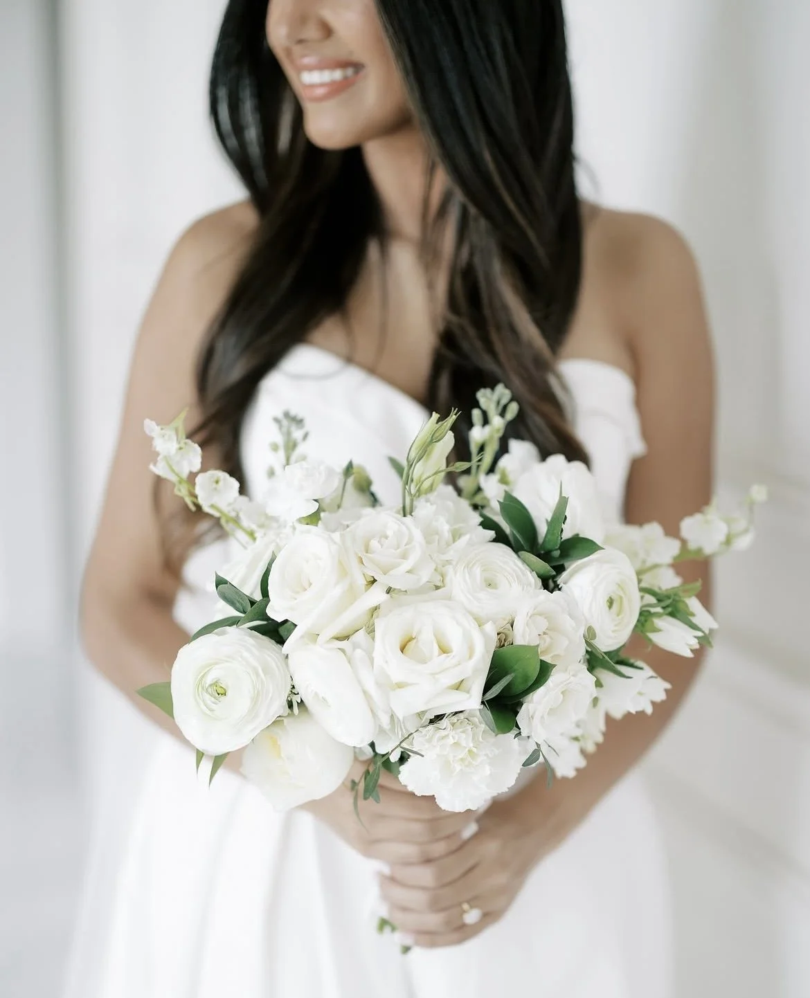 A woman in a white dress holding a bouquet of white flowers.