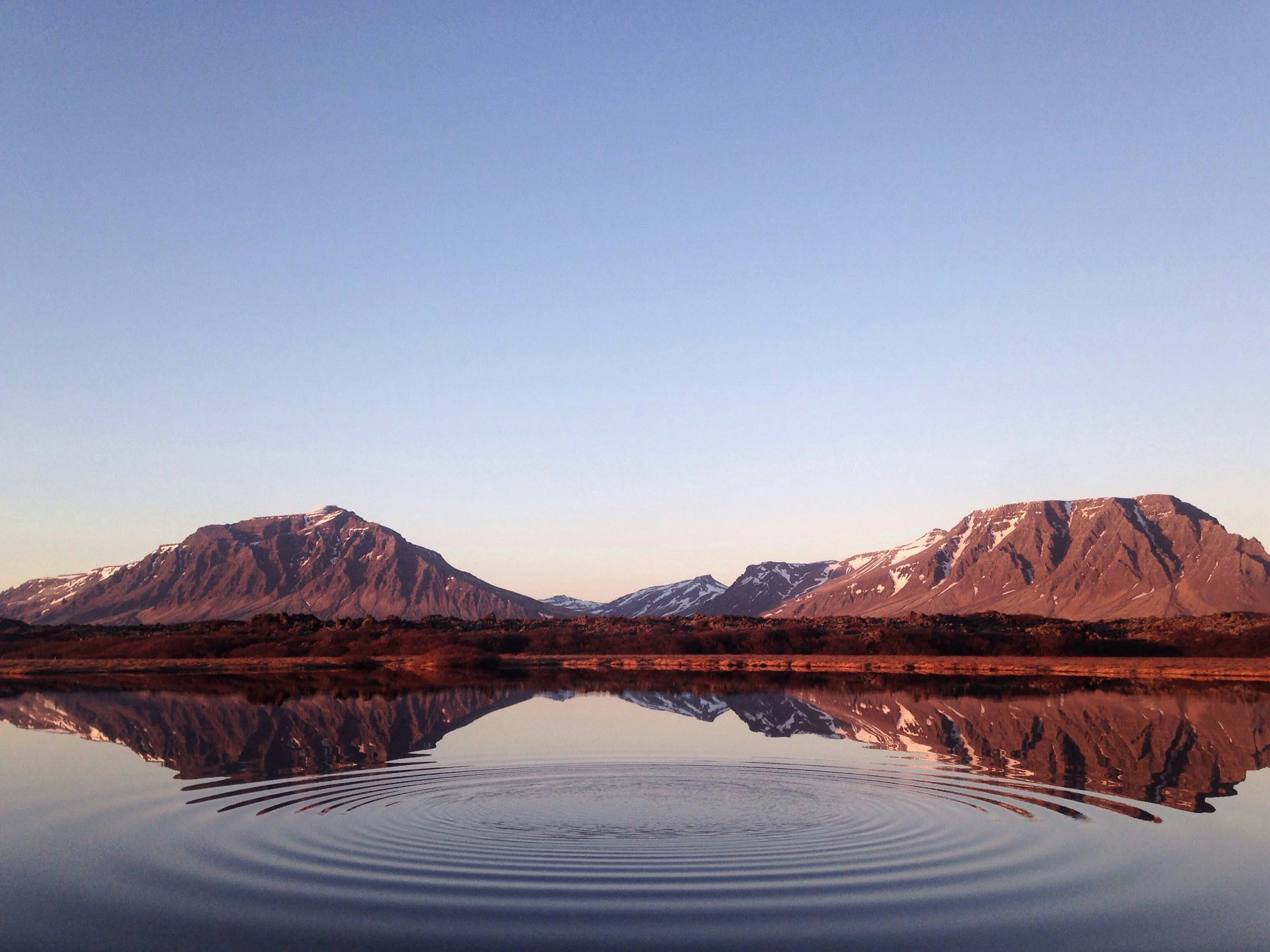 Mountains surrounding a calm lake with clear reflections of the mountains and the sky, and snow patches on the mountains.