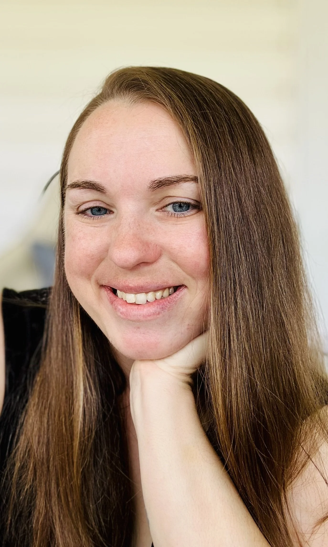 Close-up of a smiling woman with long red hair, blue eyes, and fair skin, resting her chin on her hand.