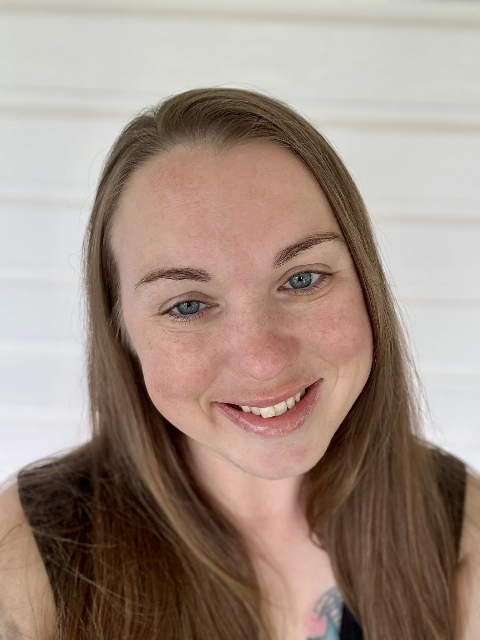 Close-up of a woman with long brown hair, blue eyes, and a big smile showing her teeth, against a white background.