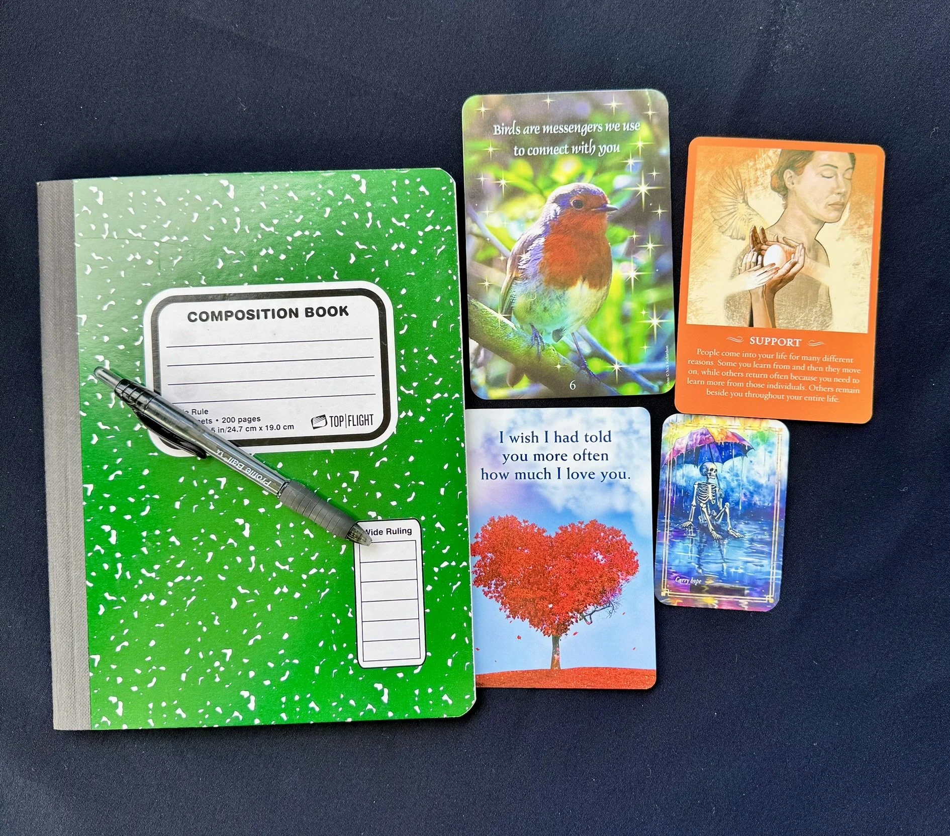 A collection of tarot and mediumship cards laid out on a dark surface, featuring images of skeletons, a girl sitting on a bench, a rainbow skull, and a colorful skeleton playing guitar, with some cards displaying messages and symbols.