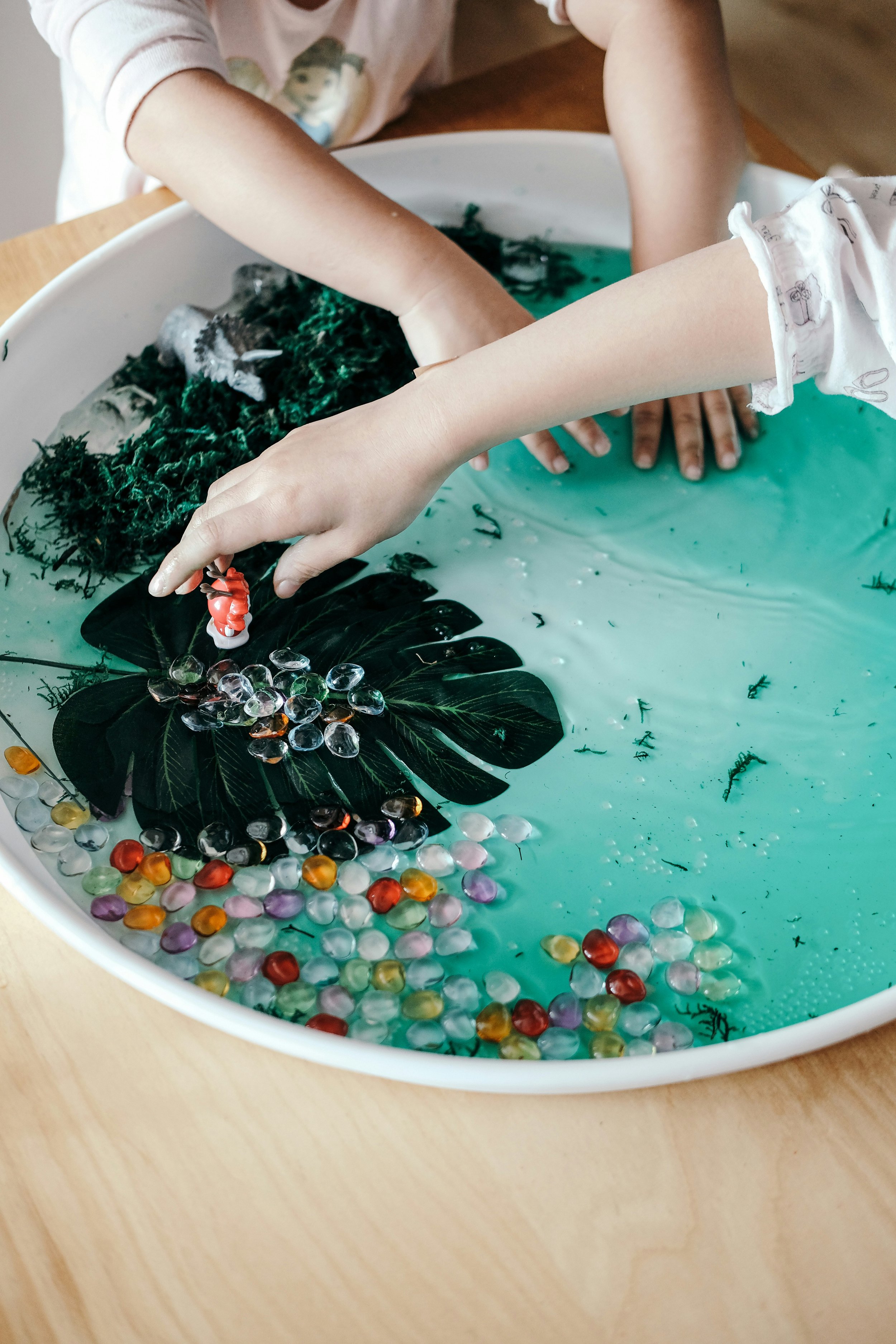 Children's hands engaging in sensory play with water beads and decorations in a sensory tray.