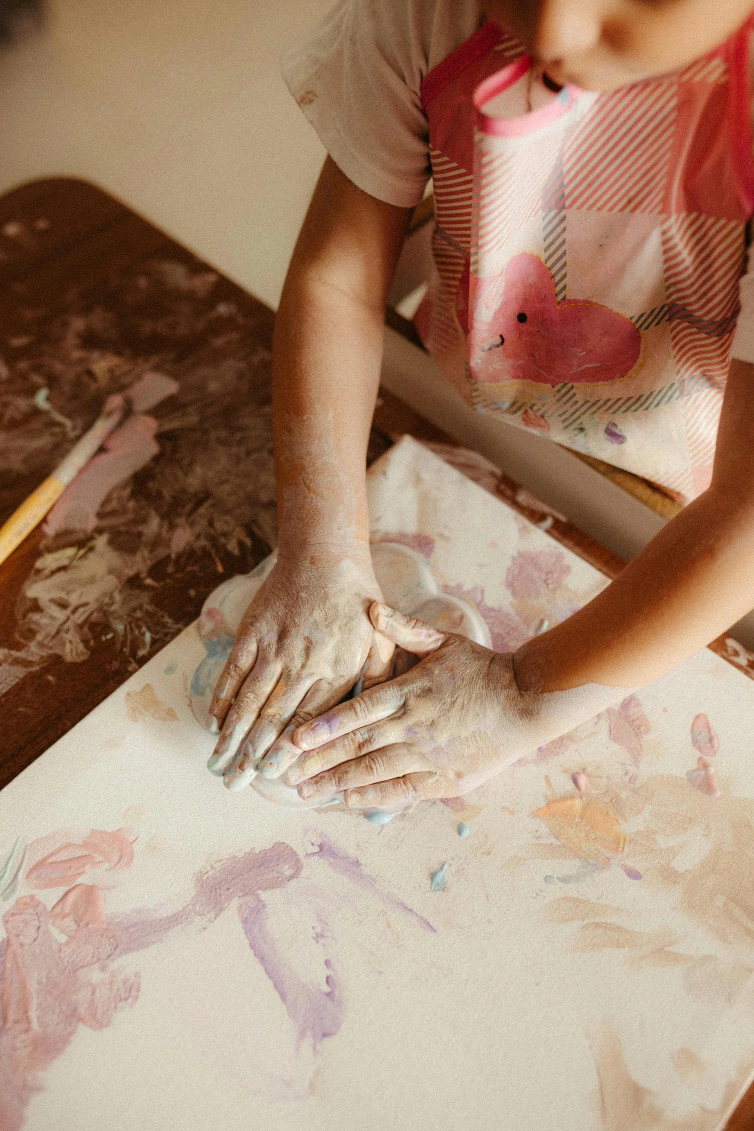 A child with painted hands pressing clay on a painted paper surface.