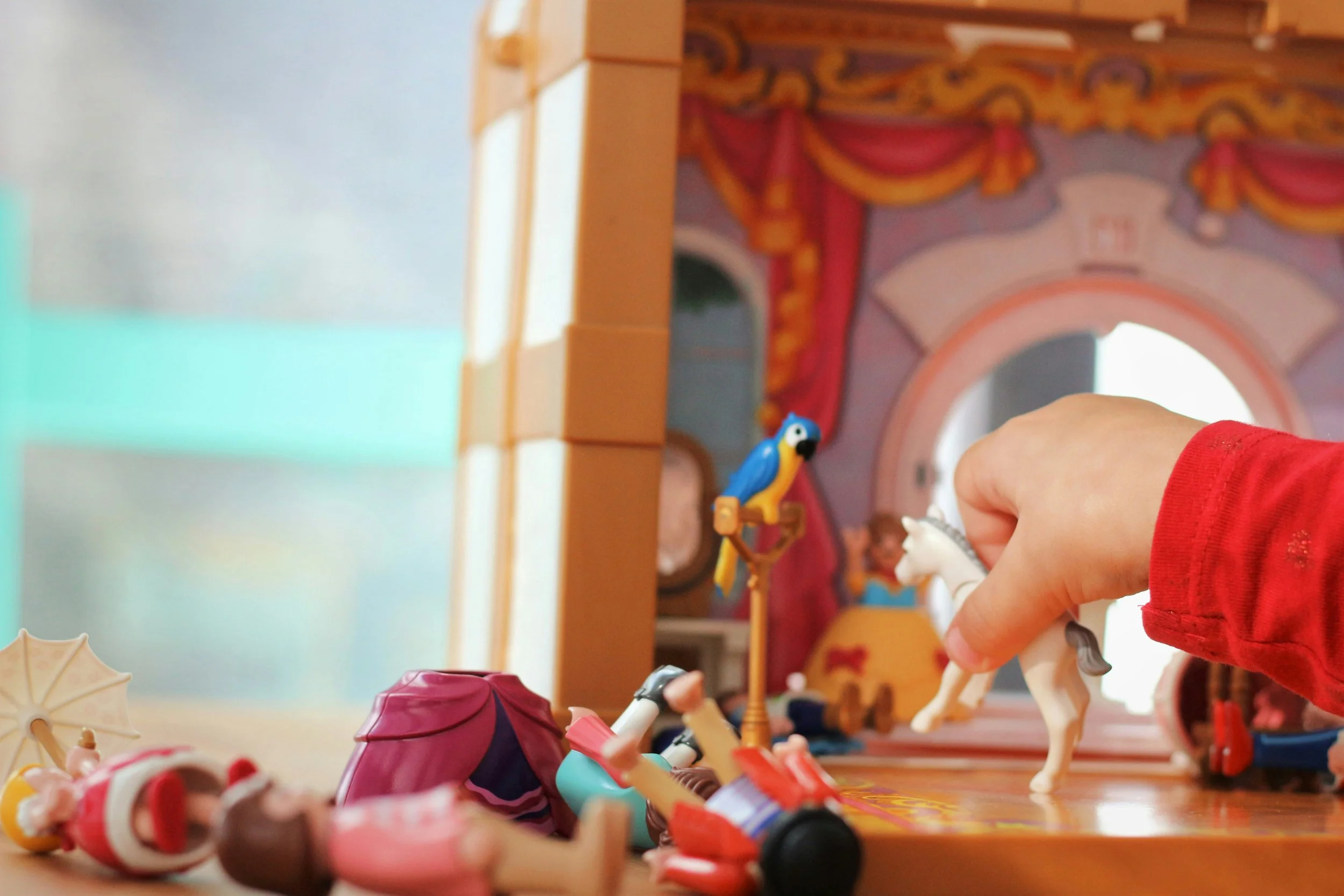 Child playing with toy animals and accessories on a wooden surface, with a colorful Circus-themed backdrop and some toys scattered around.