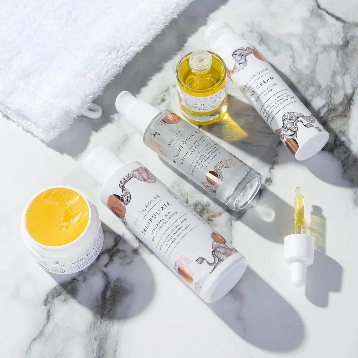 Jane Scrivner skincare products including a cleanser, a daily exfoliator, a skin elixir and moisutiring cream on a white marble surface.