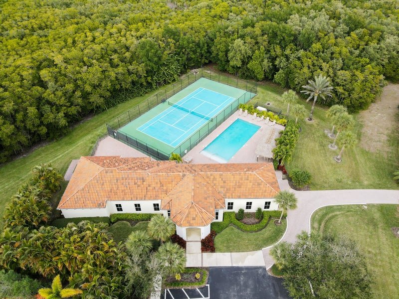 Aerial view of a residential property with a large house, tennis court, and swimming pool surrounded by lush greenery and trees.