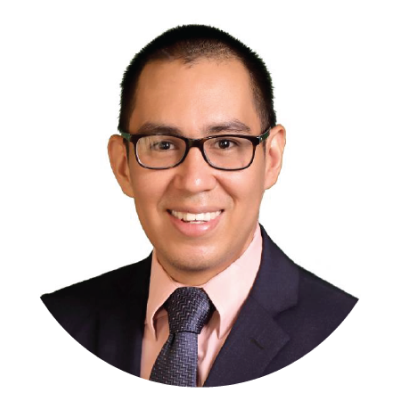 Headshot of a smiling man wearing glasses, a dark suit, pink shirt, and dark tie, against a white background.