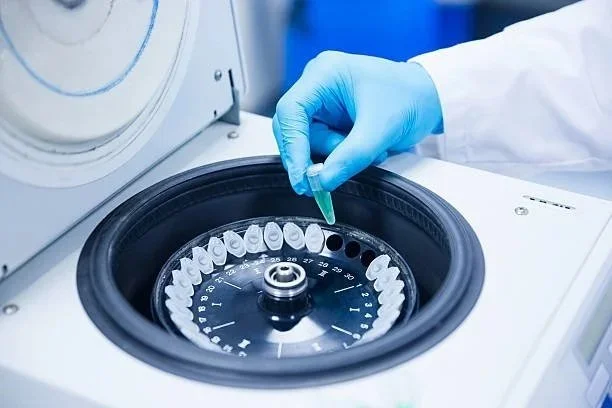 A gloved hand inserting a sample tube into a centrifuge machine.
