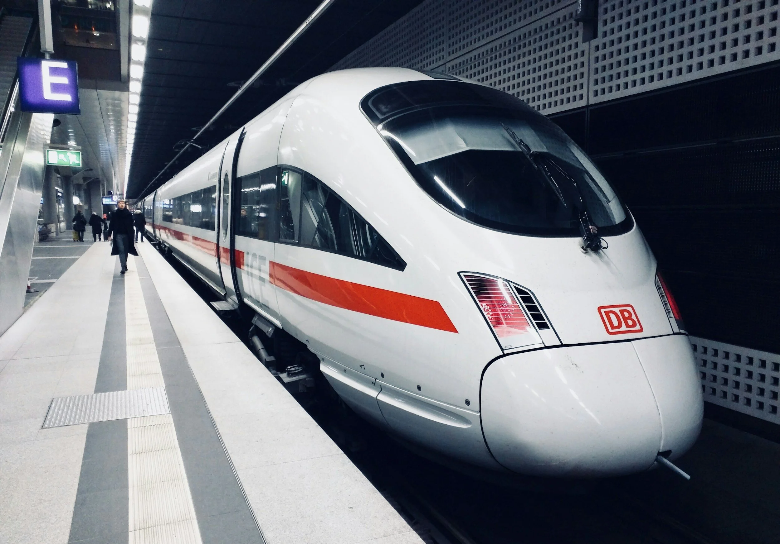 Modern high-speed train with a sleek, aerodynamic design at a station platform, with passengers walking nearby.