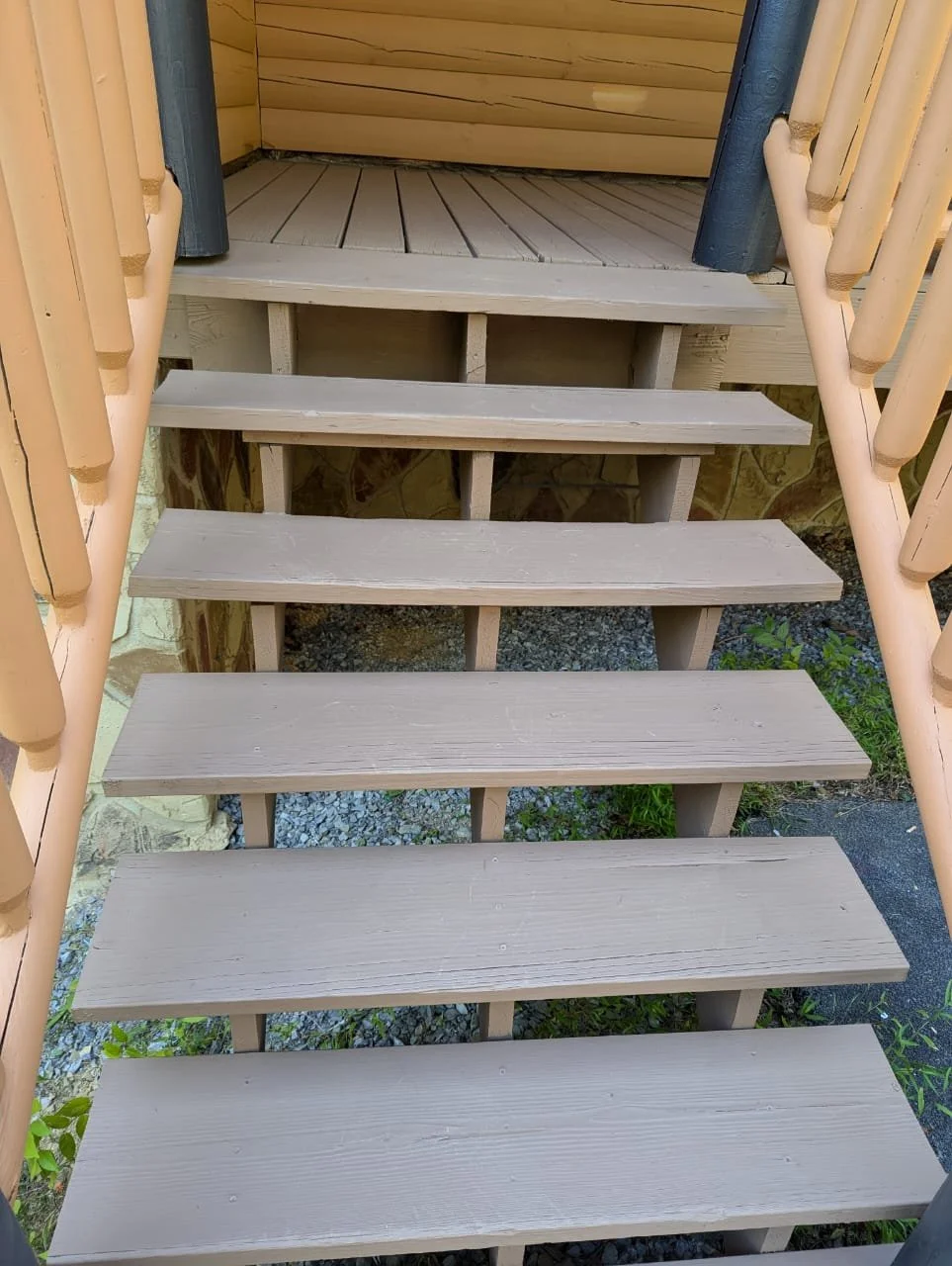 View of outdoor wooden staircase with steps leading up to a small platform, with railings on both sides and a gravel ground underneath.