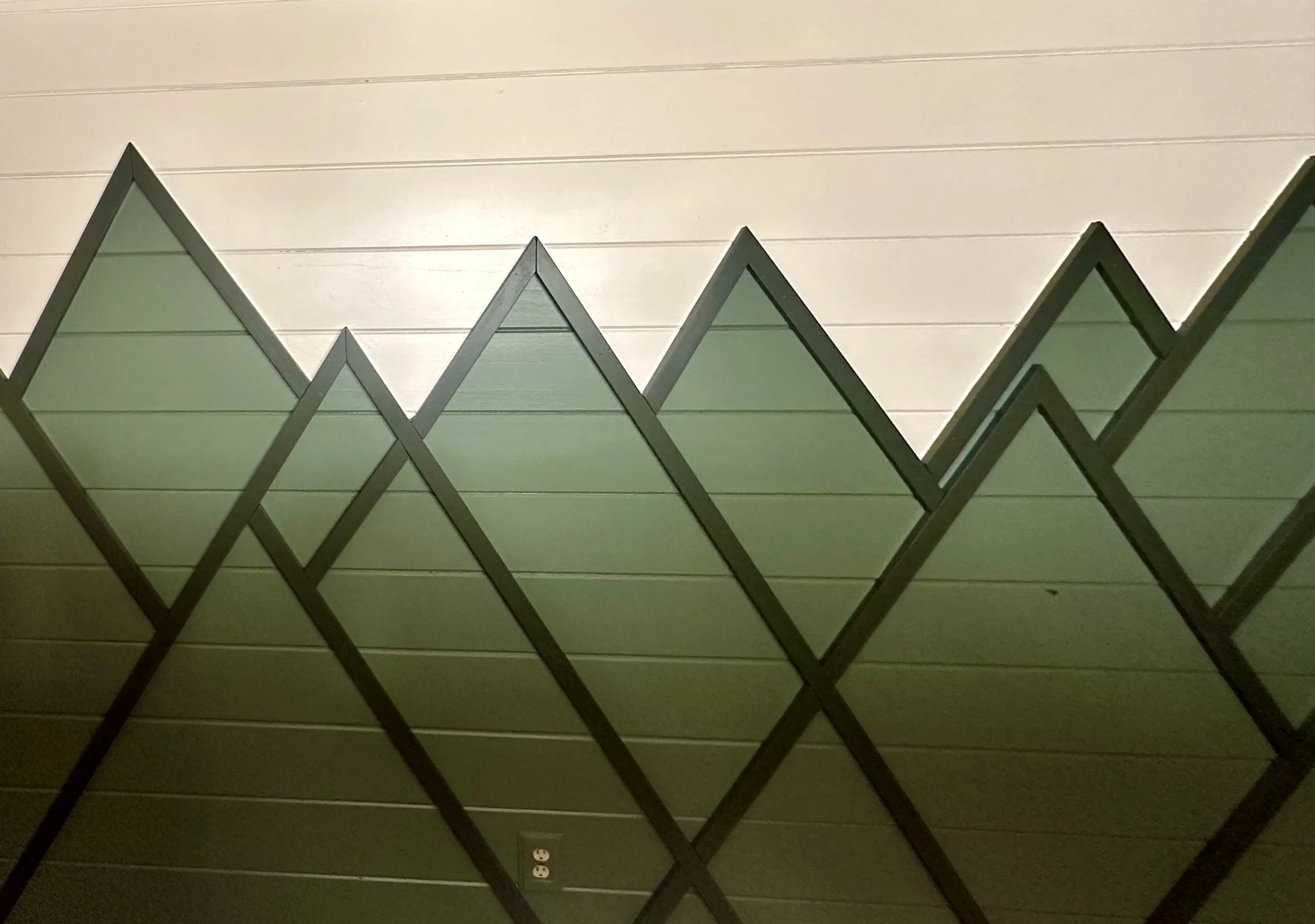 View of a wall with horizontal paneling and electrical outlets, with a zigzag mirror hanging on it.