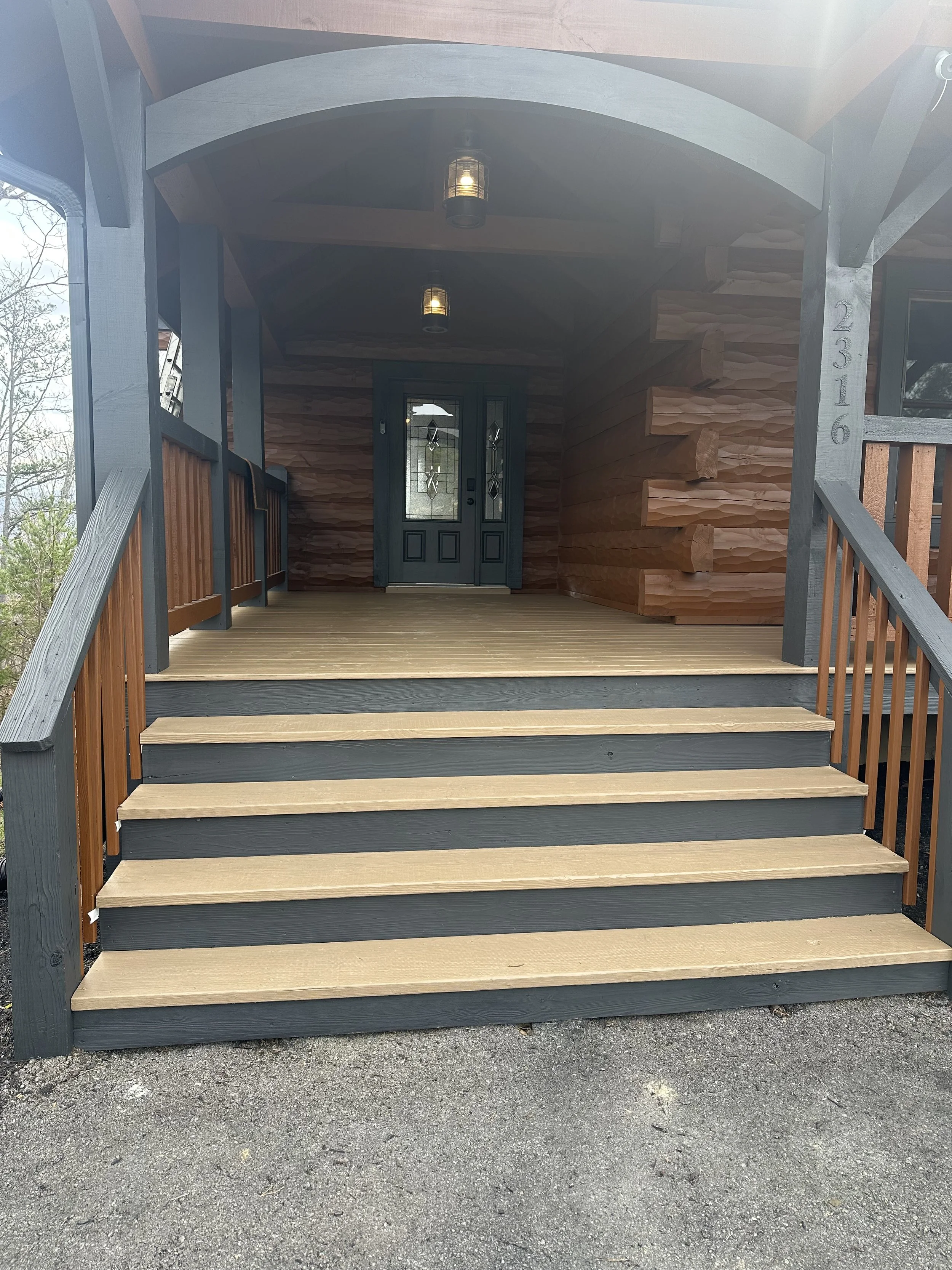 Front porch of a house with stairs leading up to a teal door, wooden siding, wooden ceiling, hanging light fixtures, and house number 2316 on the support post.