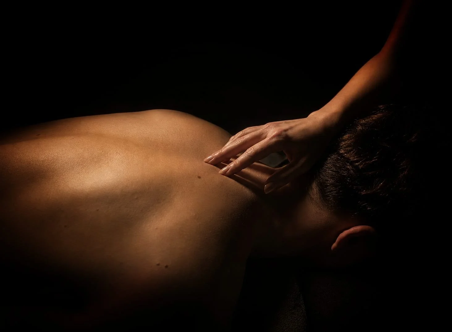 Close-up of a gentle touch on a man's back during a private sensory experience. Silence, touch and deep relaxation are at the heart of the ritual.
