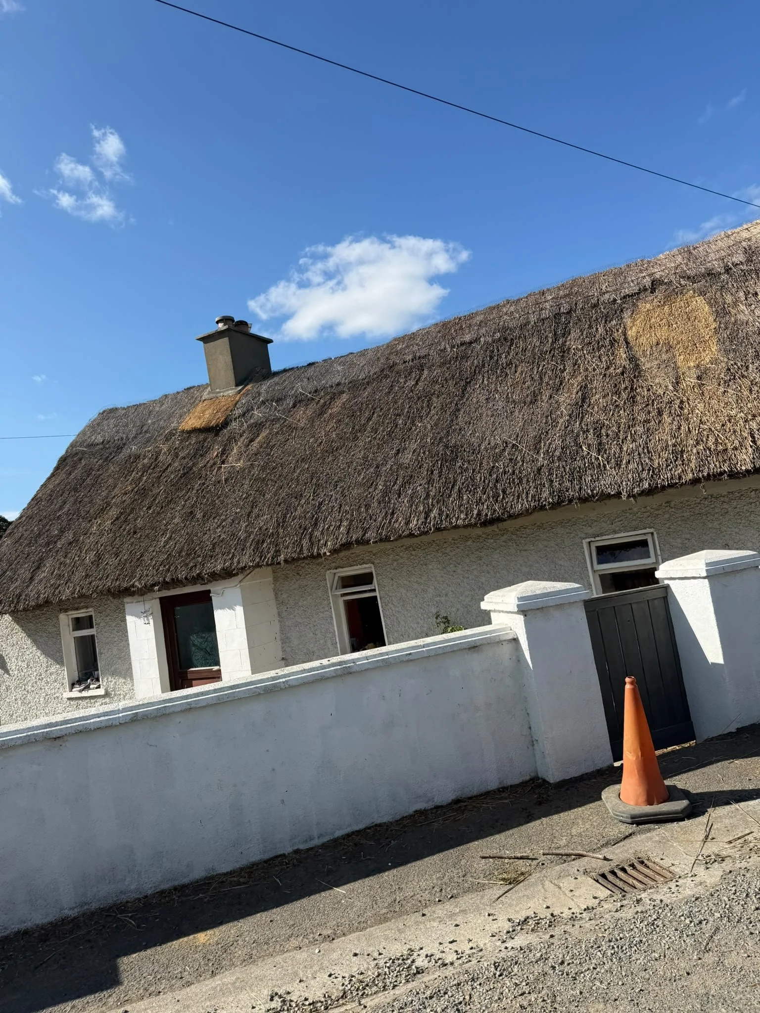 A house with a thatched roof, white walls, and small windows, with a newly repaired chimney and section below the ridge.