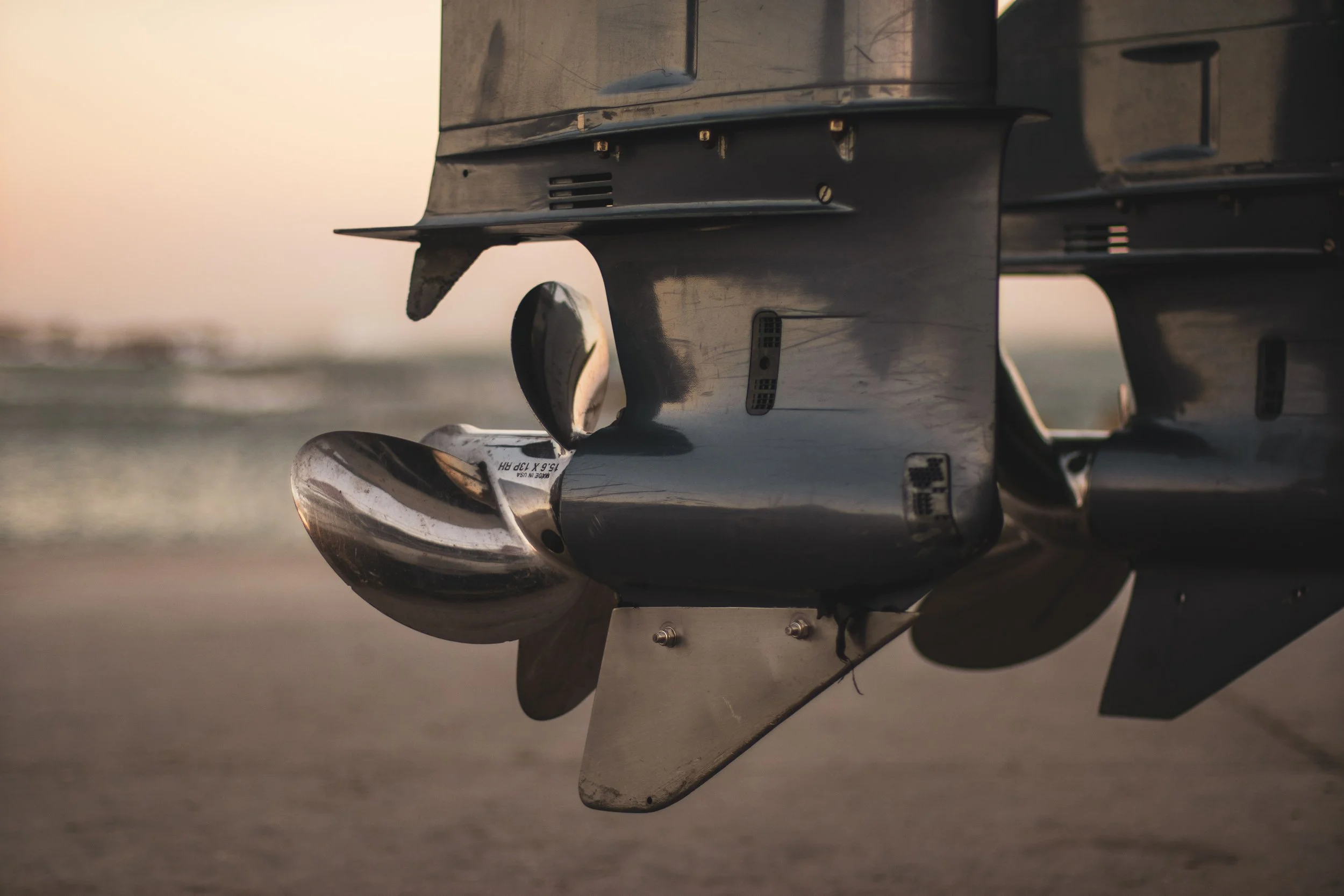 Close-up of a jet engine with a reflective metallic surface, taken at sunset over a runway.