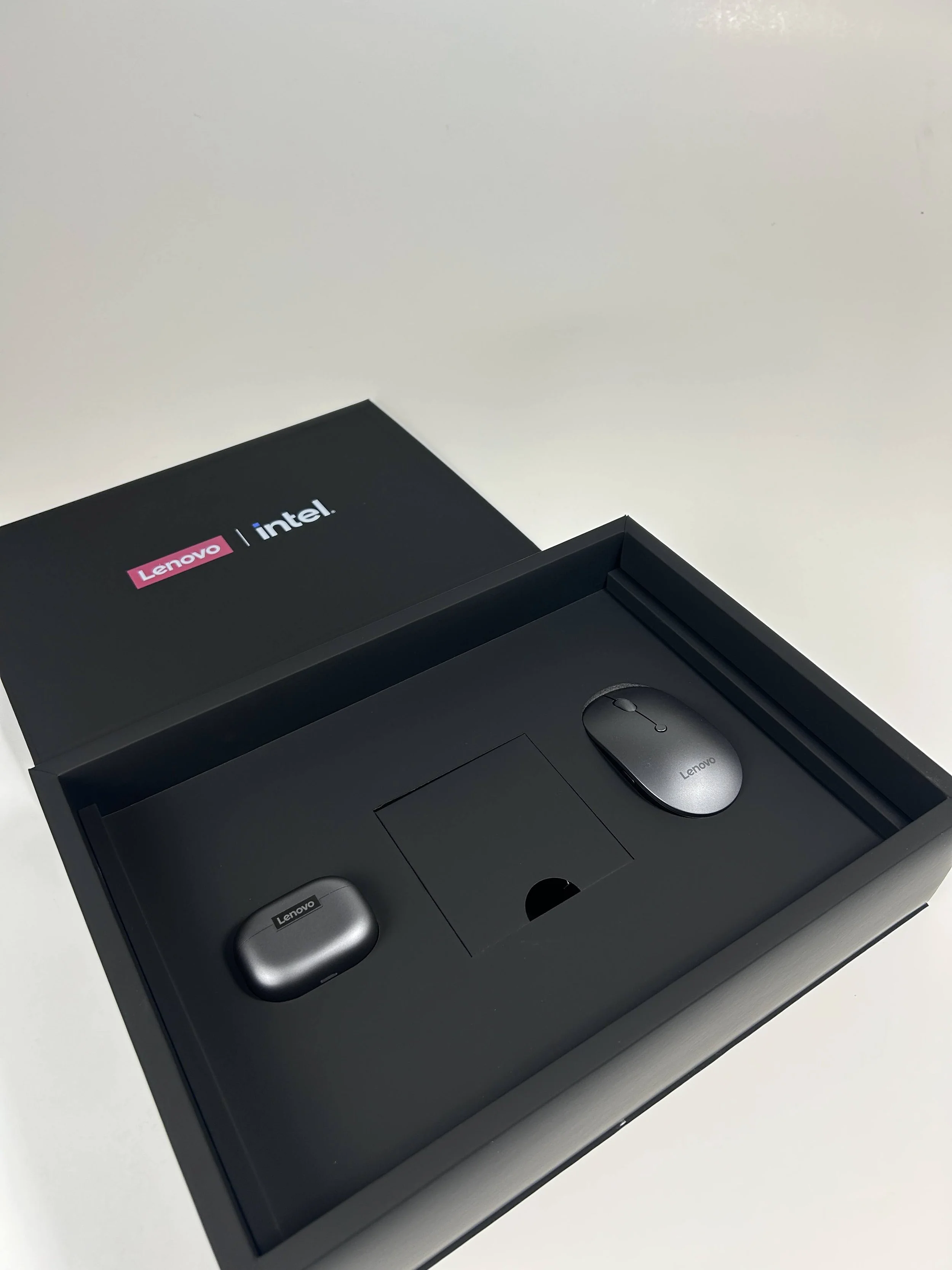 A black box with Lenovo and Intel logos contains two gray wireless earbuds and a gray wireless mouse, all resting inside foam compartments.