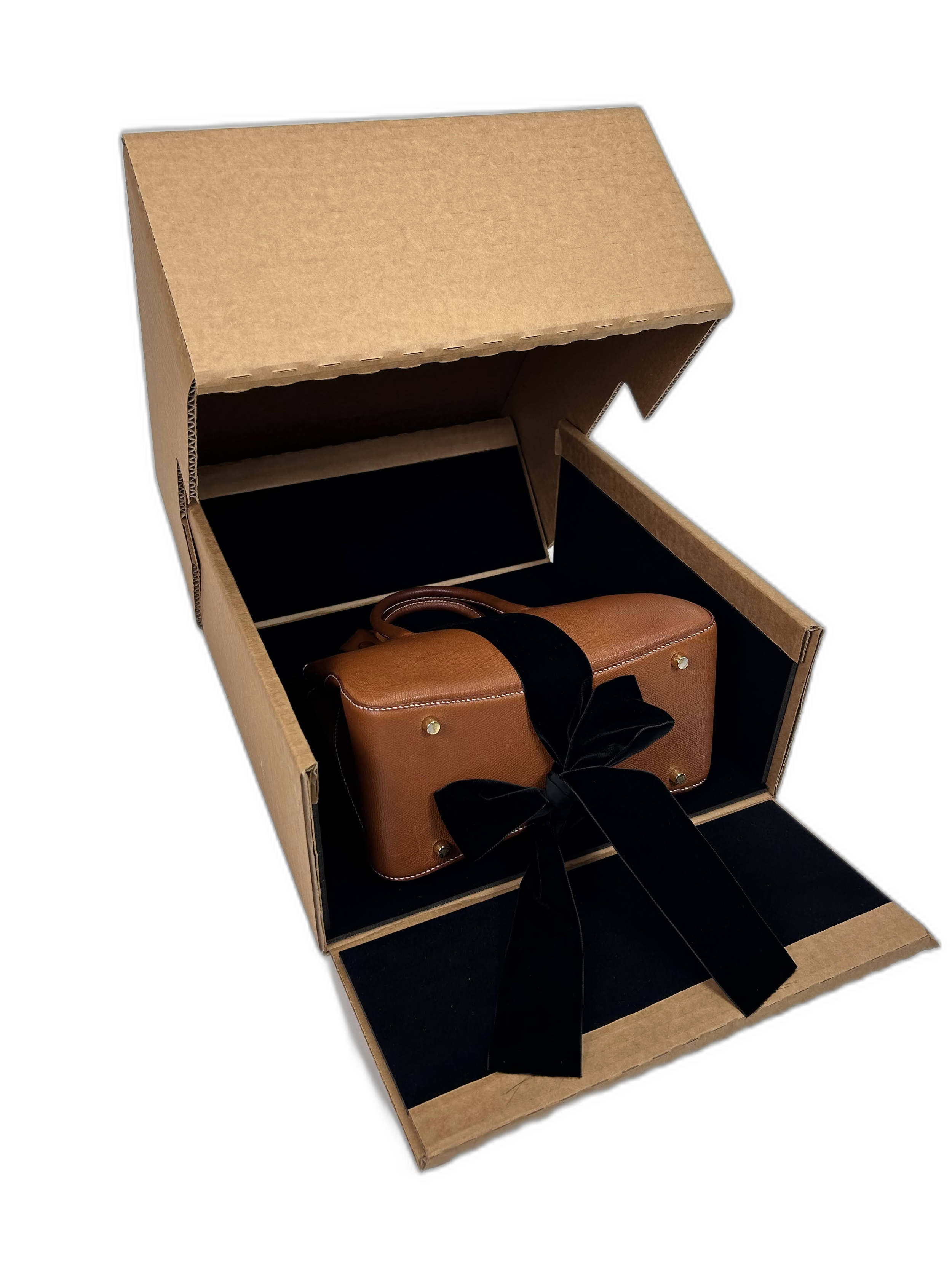 Open cardboard box with a small brown suitcase inside, black ribbons tied around the suitcase in a bow, against a black background.