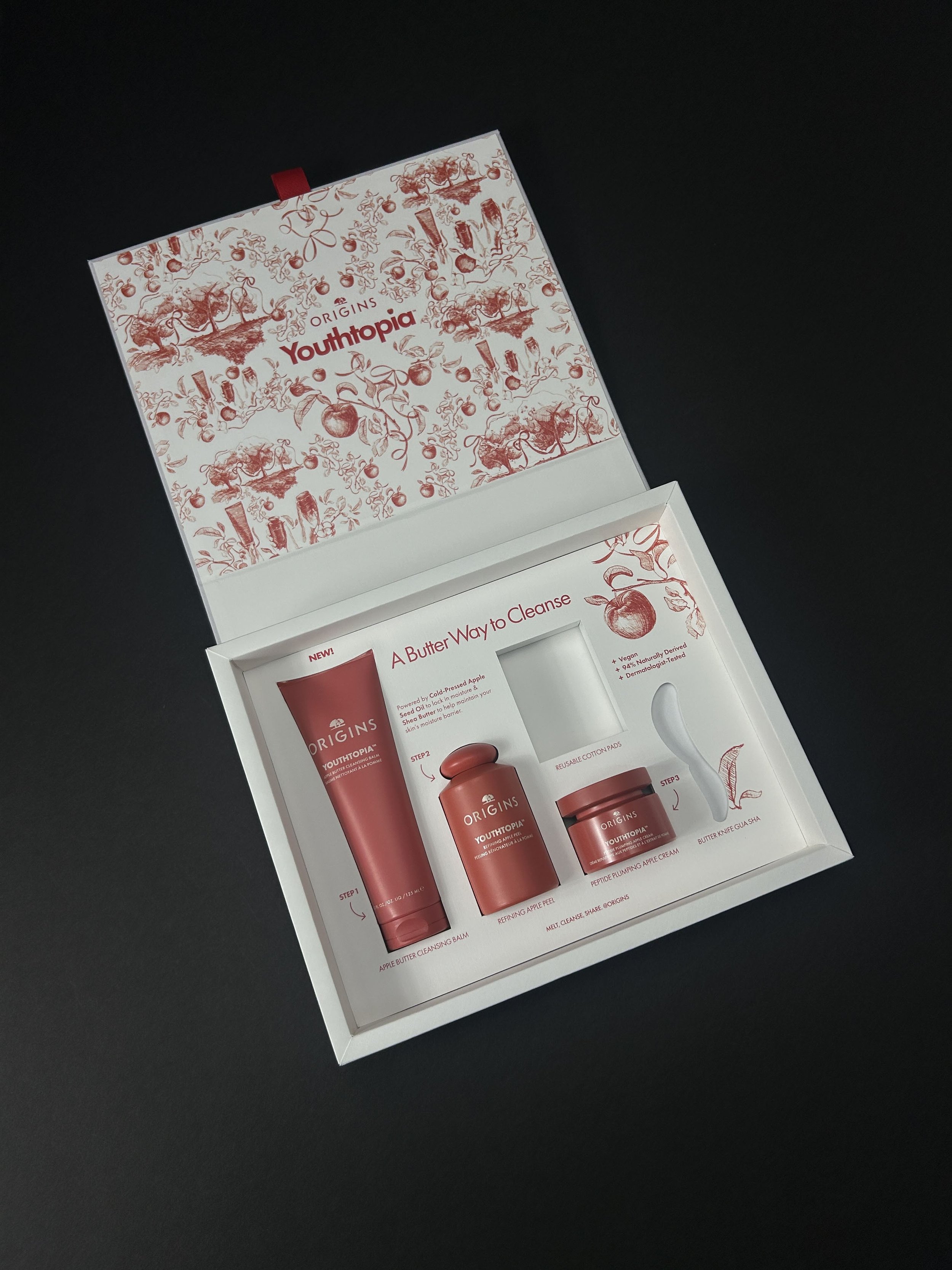 Open Origins Youthopia skincare product packaging box with various skincare products inside on a black background.