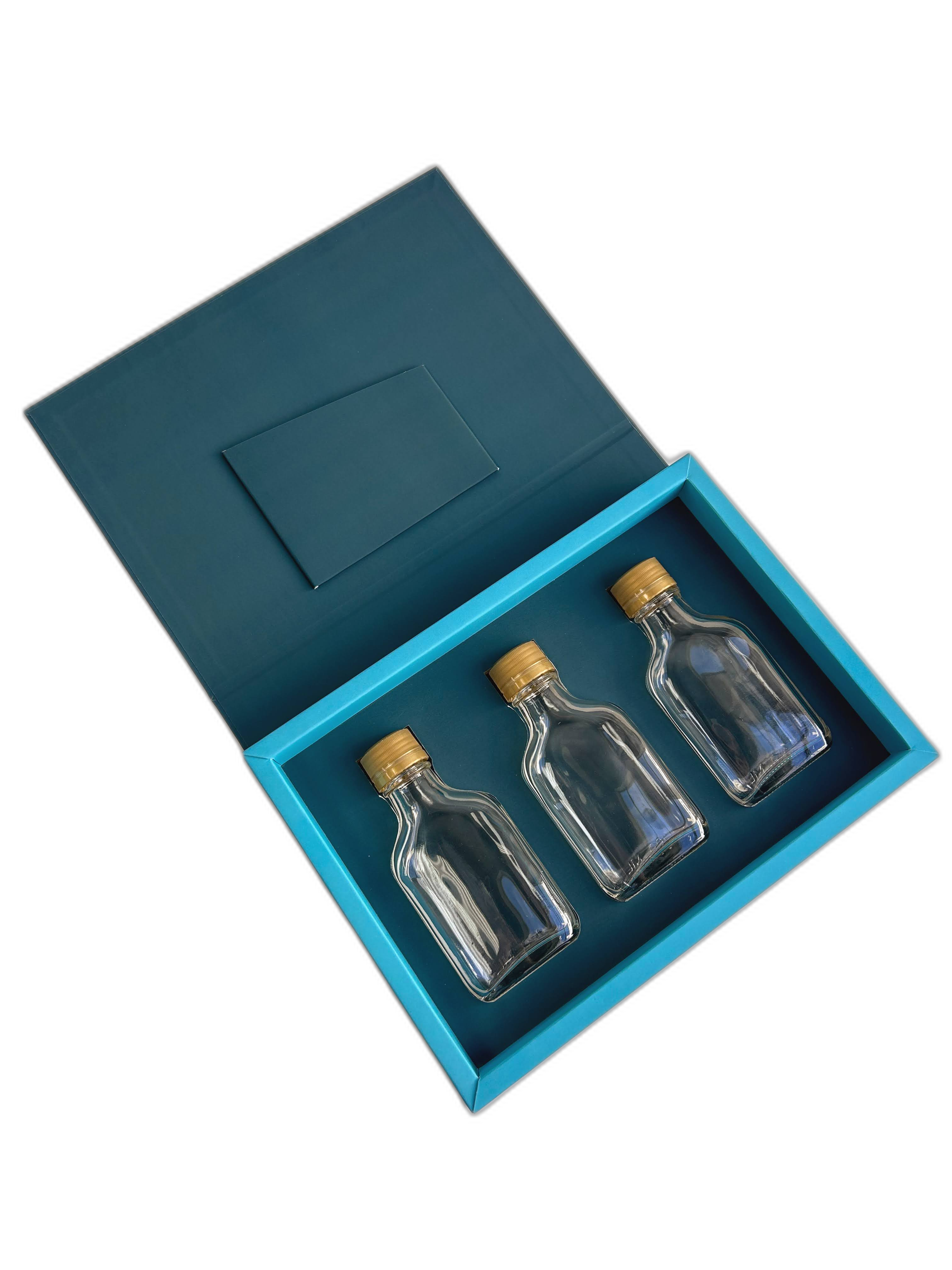 A blue box with a lid contains three small glass bottles with gold caps, arranged in a row inside the box.
