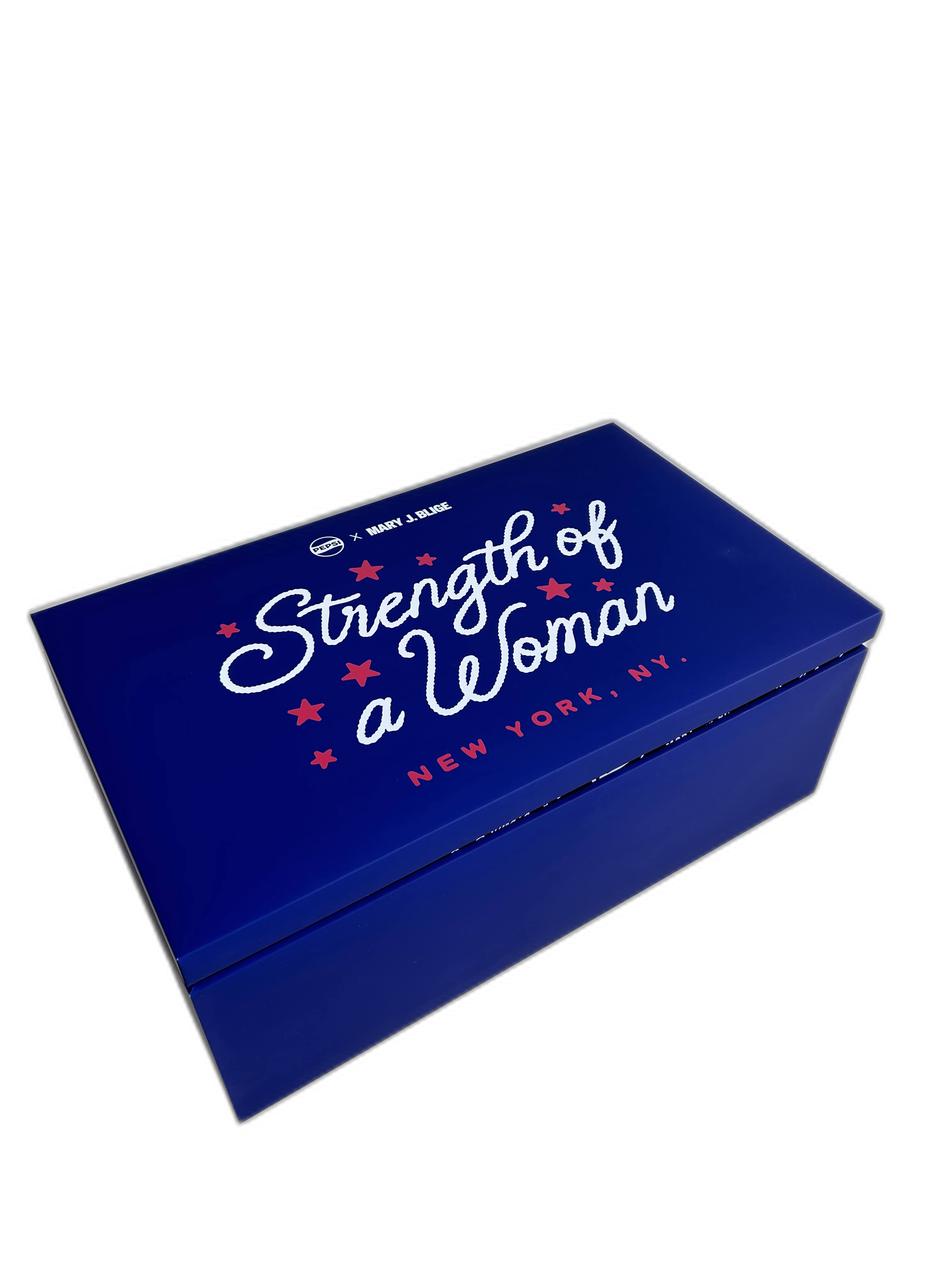 A blue box with red and white text reads 'Strength of a Woman,' featuring smaller text indicating 'New York, NY' and collaboration with Pepsi and Mary J. Blige.