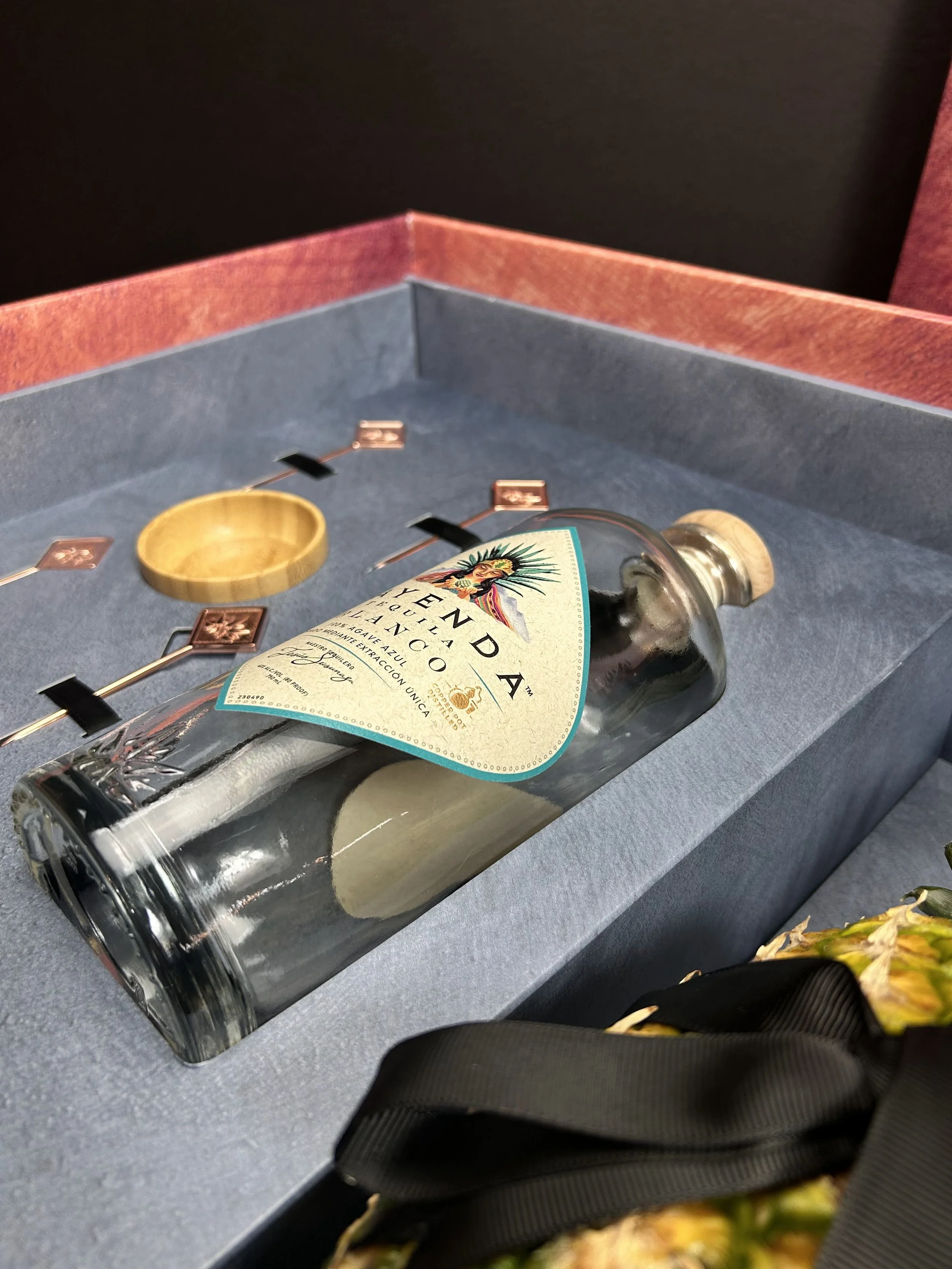 A bottle of Tequila Ocho, with a partially visible black ribbon on a gray surface.