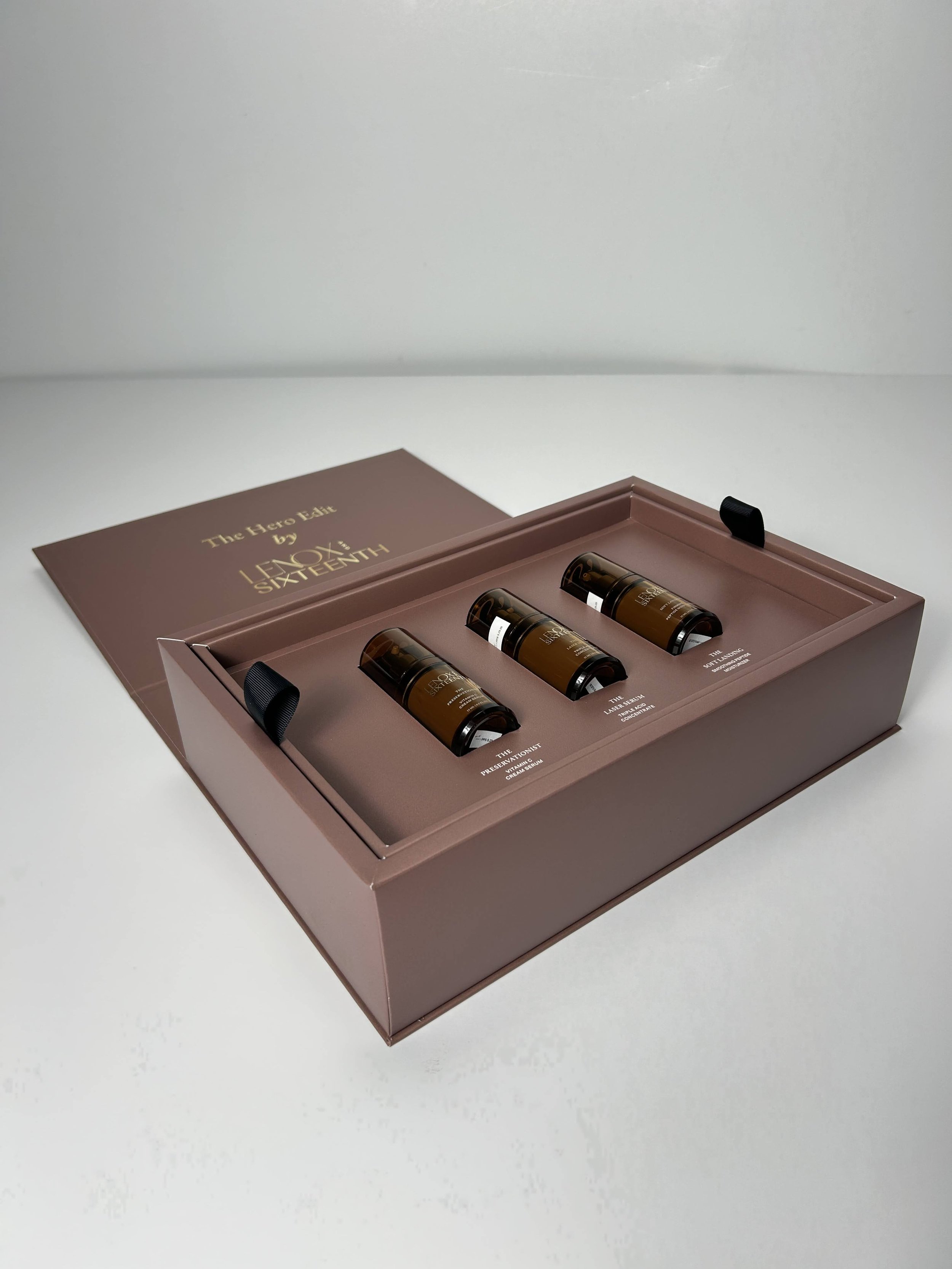 A pink box containing three skincare serum bottles labeled 'The Preservationist' and 'The Laser Serum,' with a gold foil letter and the words 'The Hero Edit by LIXU SIXTEENTH' on the lid, on a white surface.