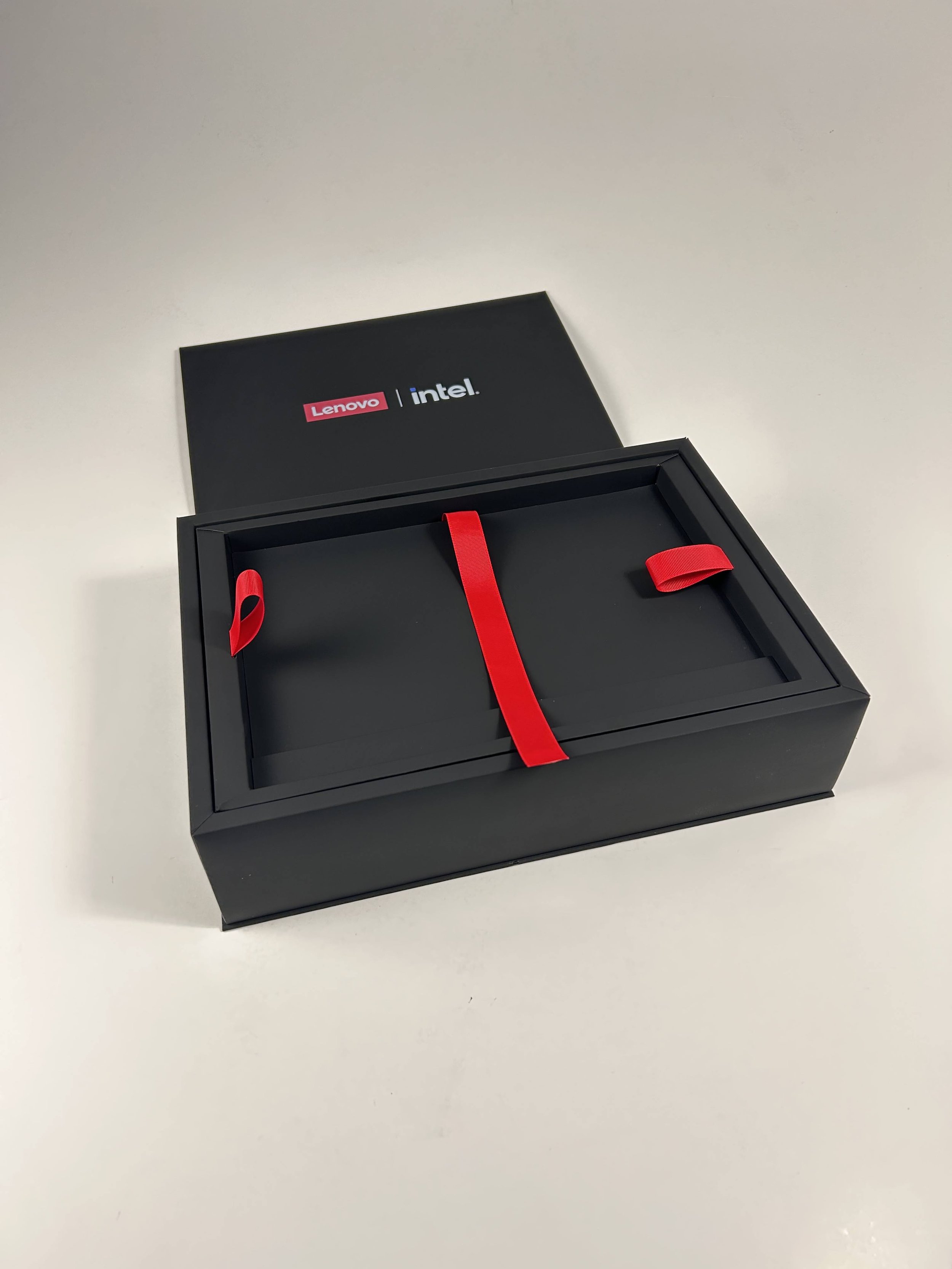 Black gift box with red ribbon and a black lid with Lenovo and Intel logos, placed on a white surface.