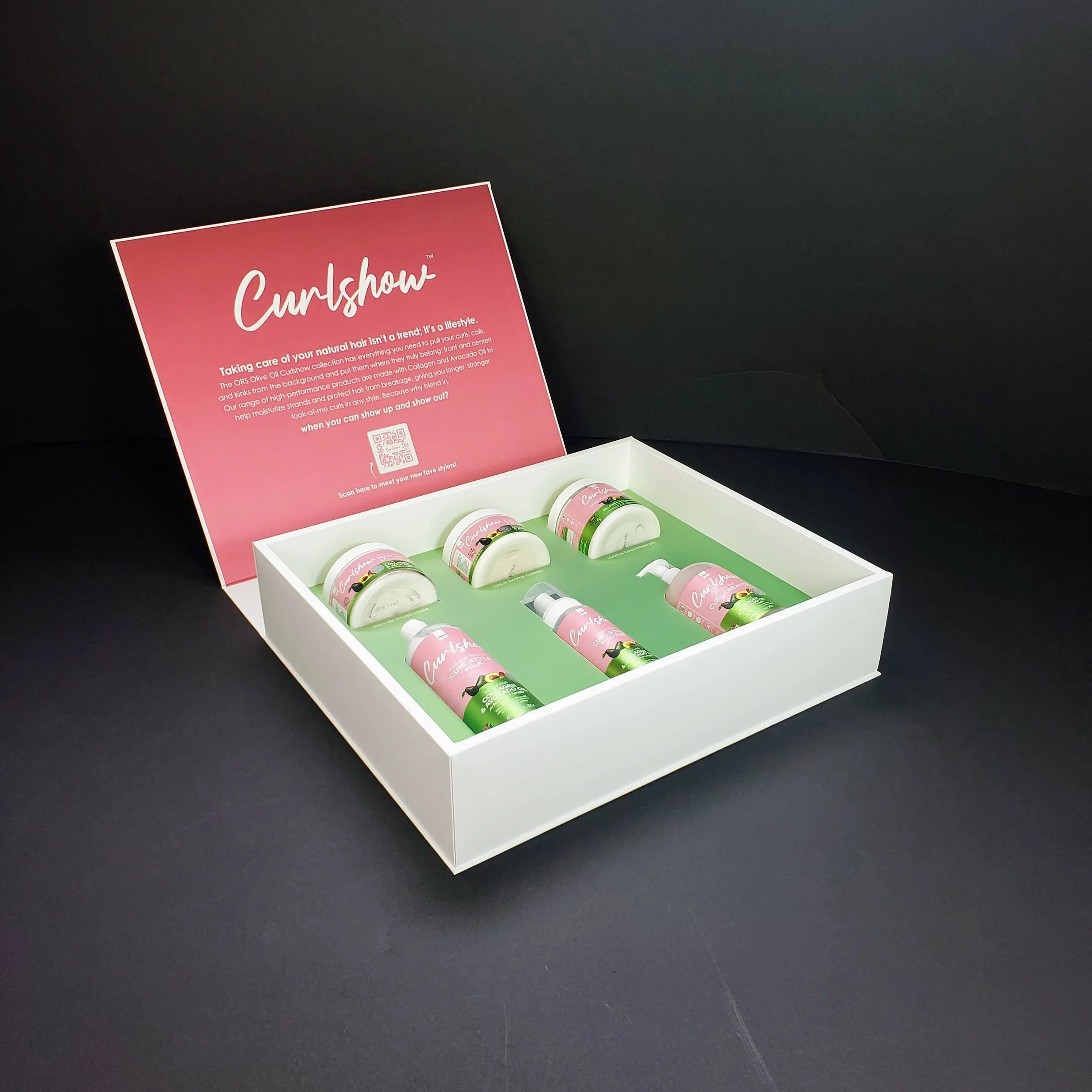 A display box with bottles of Curlshow hair product, featuring pink and green labels, on a black surface with a pink informational sign behind it.