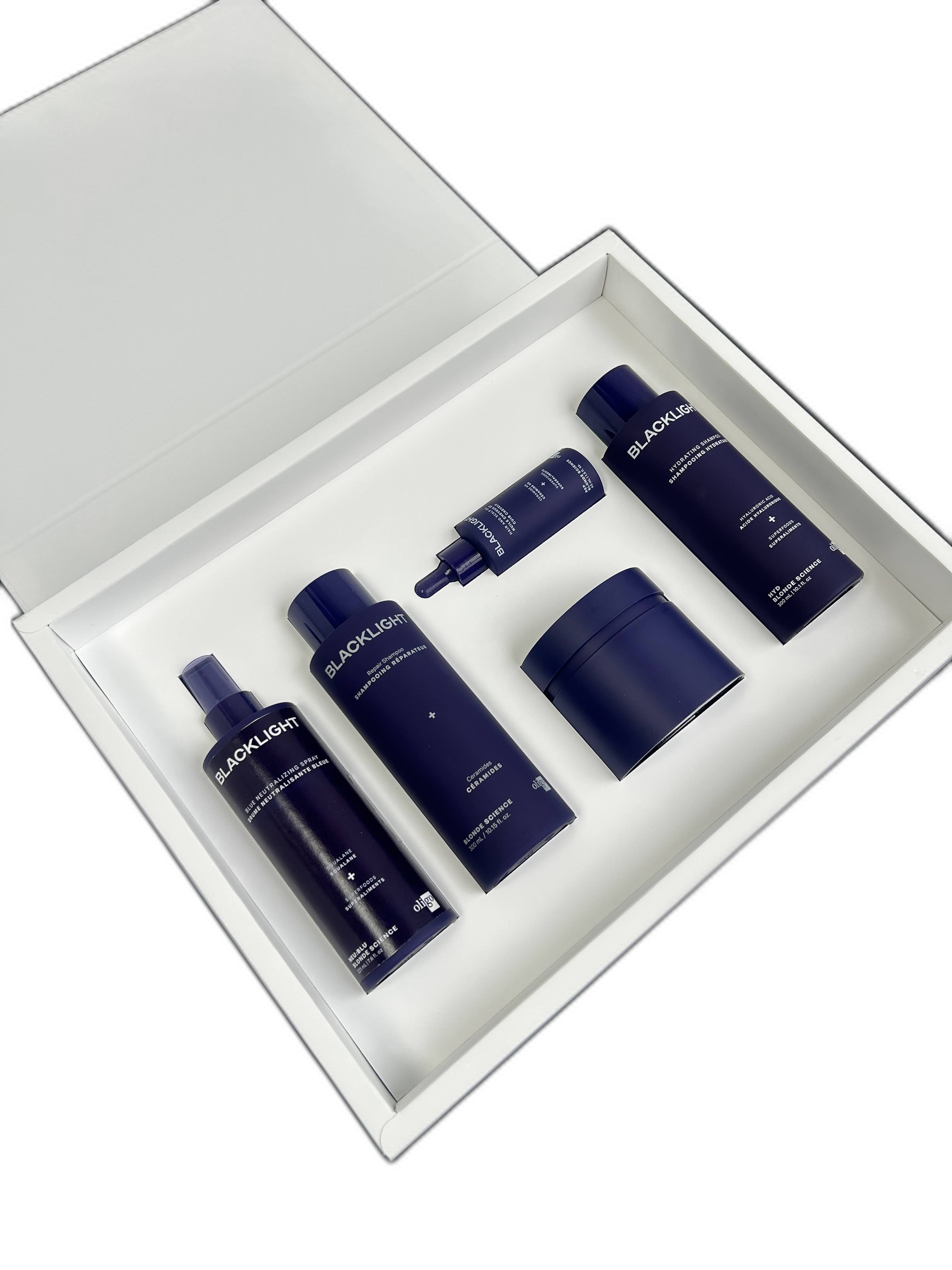 A white box containing four dark blue bottles and containers of hair care products from the Blacklight brand, with various sizes and shapes, including spray bottles and jars.
