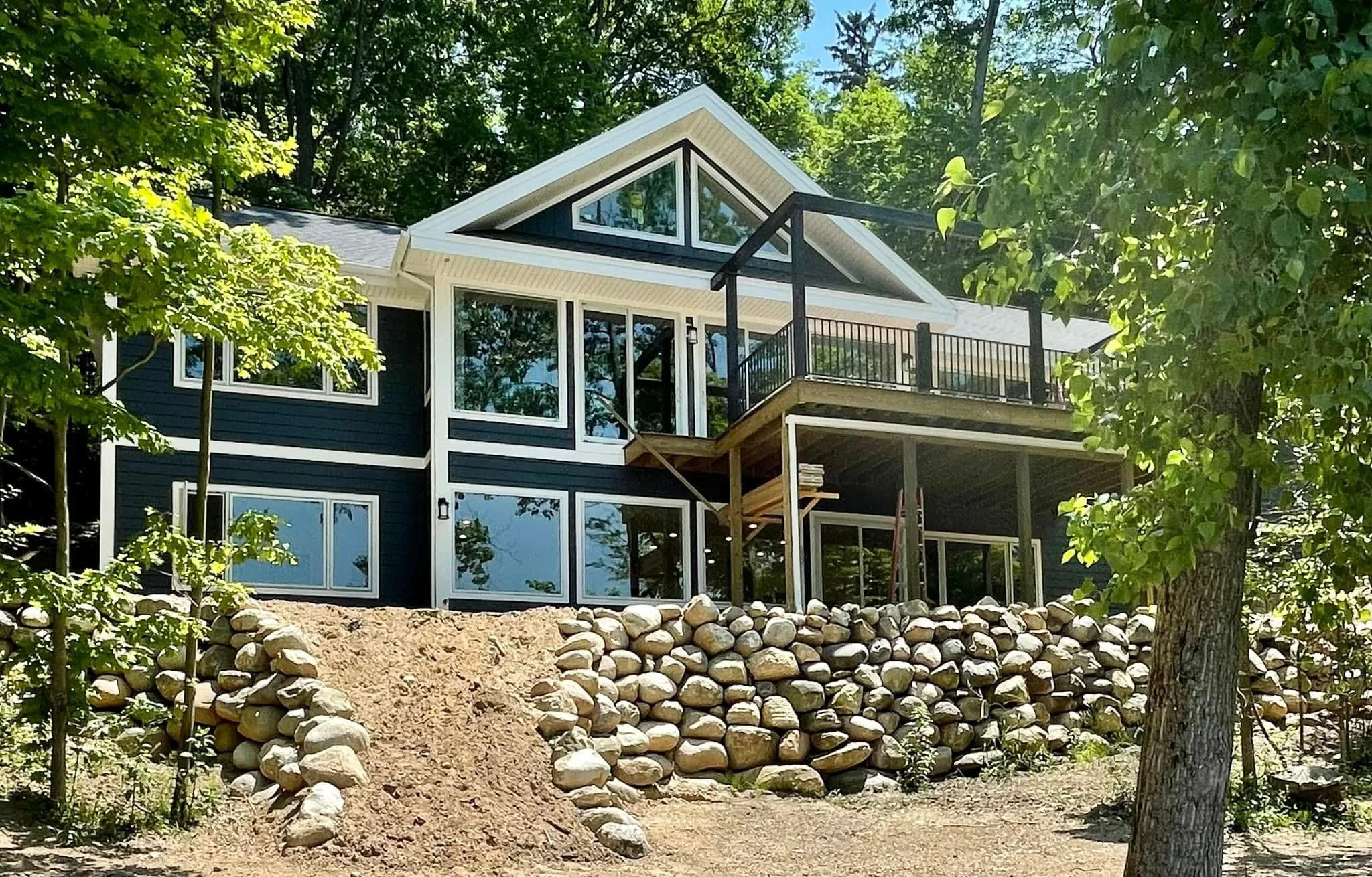 A modern house with large windows and a balcony, surrounded by trees and a rock landscape.