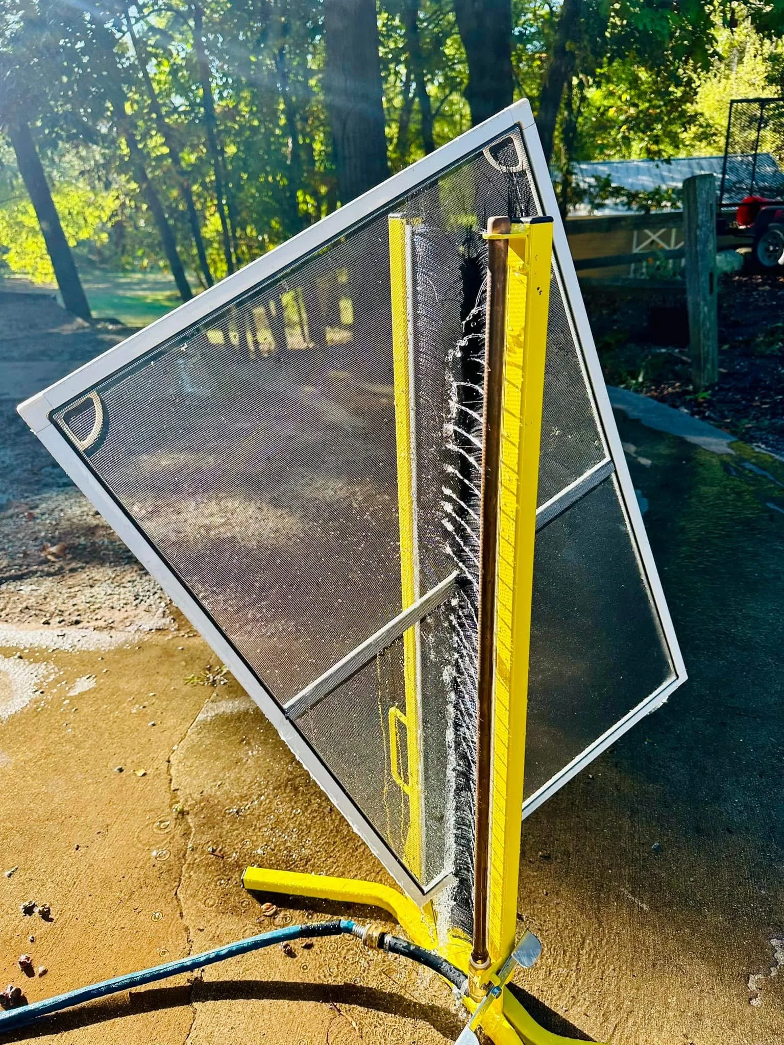 A water-filled chalkboard with a yellow measuring stick, positioned on a dirt ground outdoors, with a hose on the ground and trees in the background.